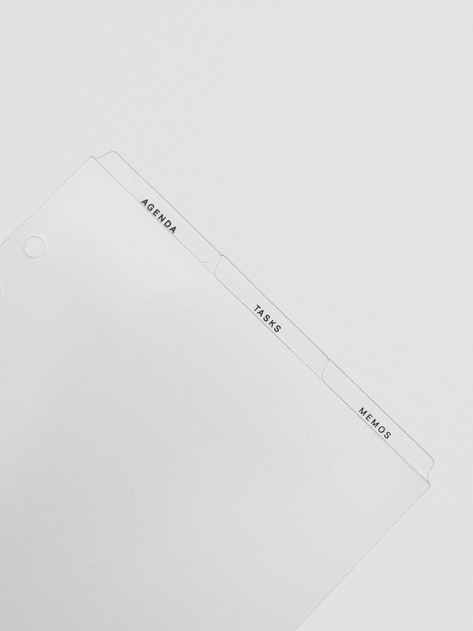 Angled close-up of the ultra-thin clear planner dividers showing top tabs labeled Agenda, Tasks, and Memos.