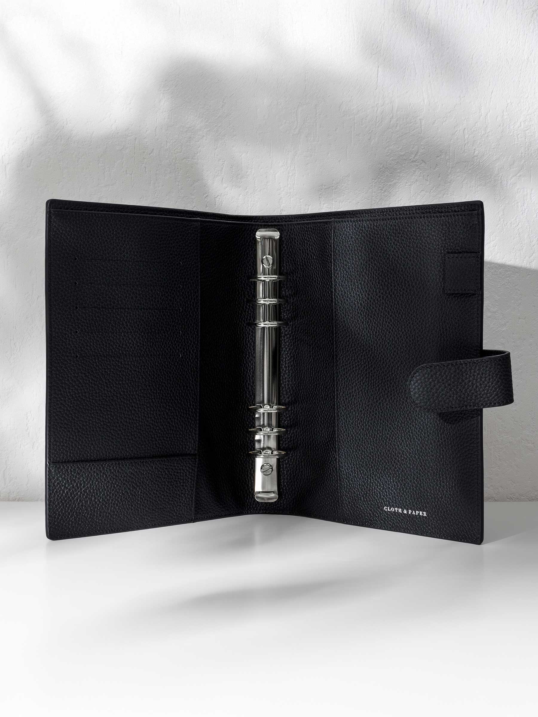 Black leather agenda displayed against a shadowed background. It is opened to show off the silver hardware and company logo stamp.