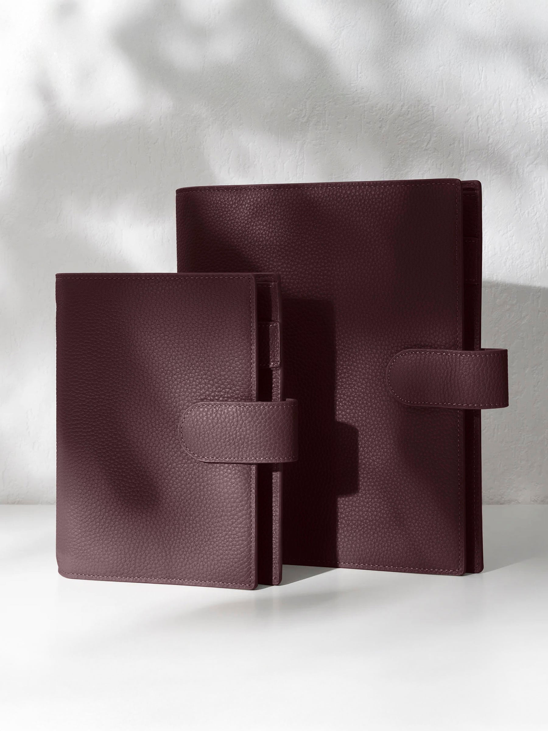 Two dark burgundy leather agendas displayed against a shadowed background.