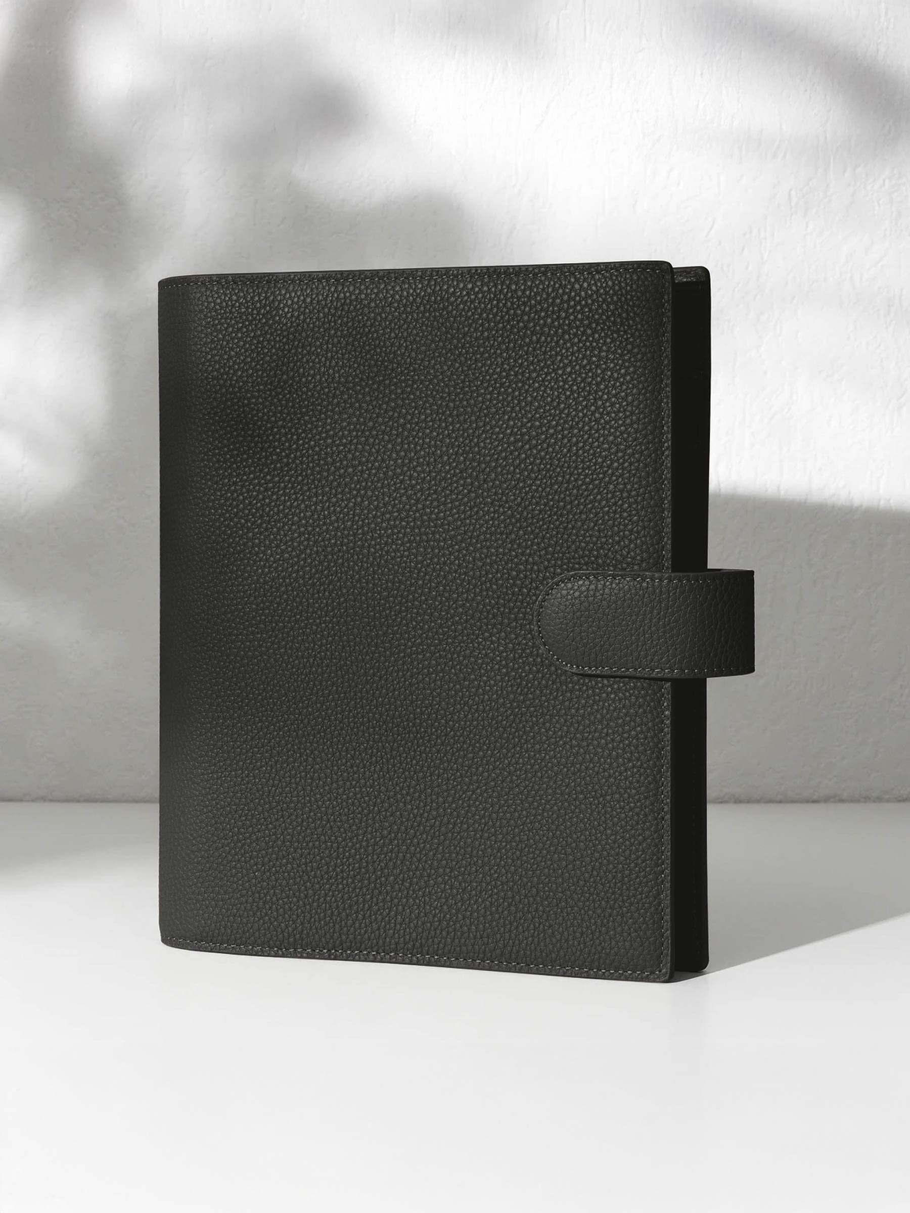 A closed cafenoir leather planner with a closure displayed against a shadowed background.