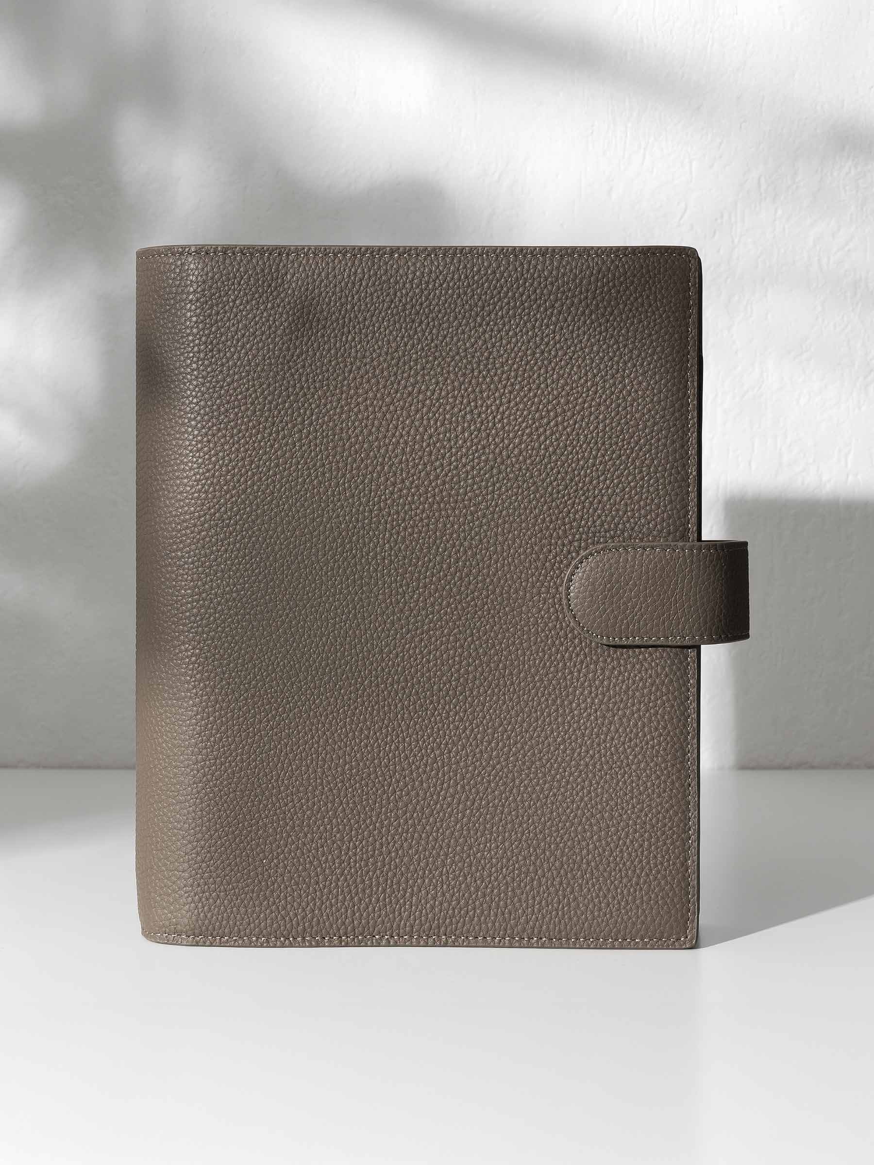 A closed cortado leather planner with a closure displayed against a shadowed background.