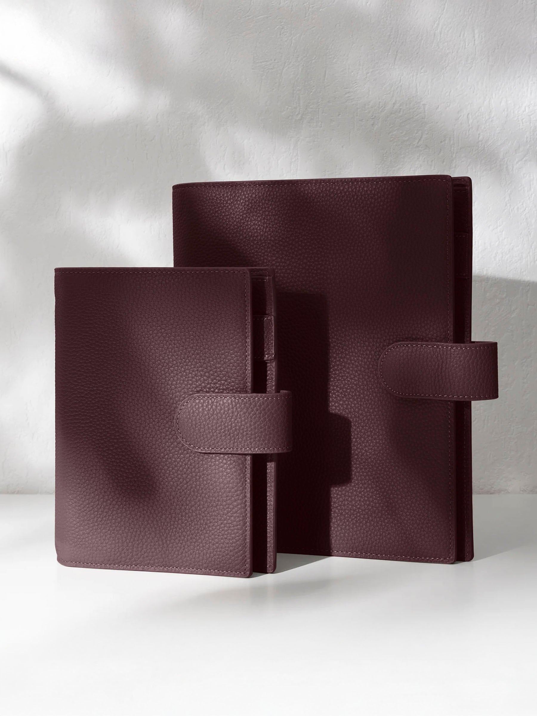 Two dark burgundy leather agendas on an off-white background.