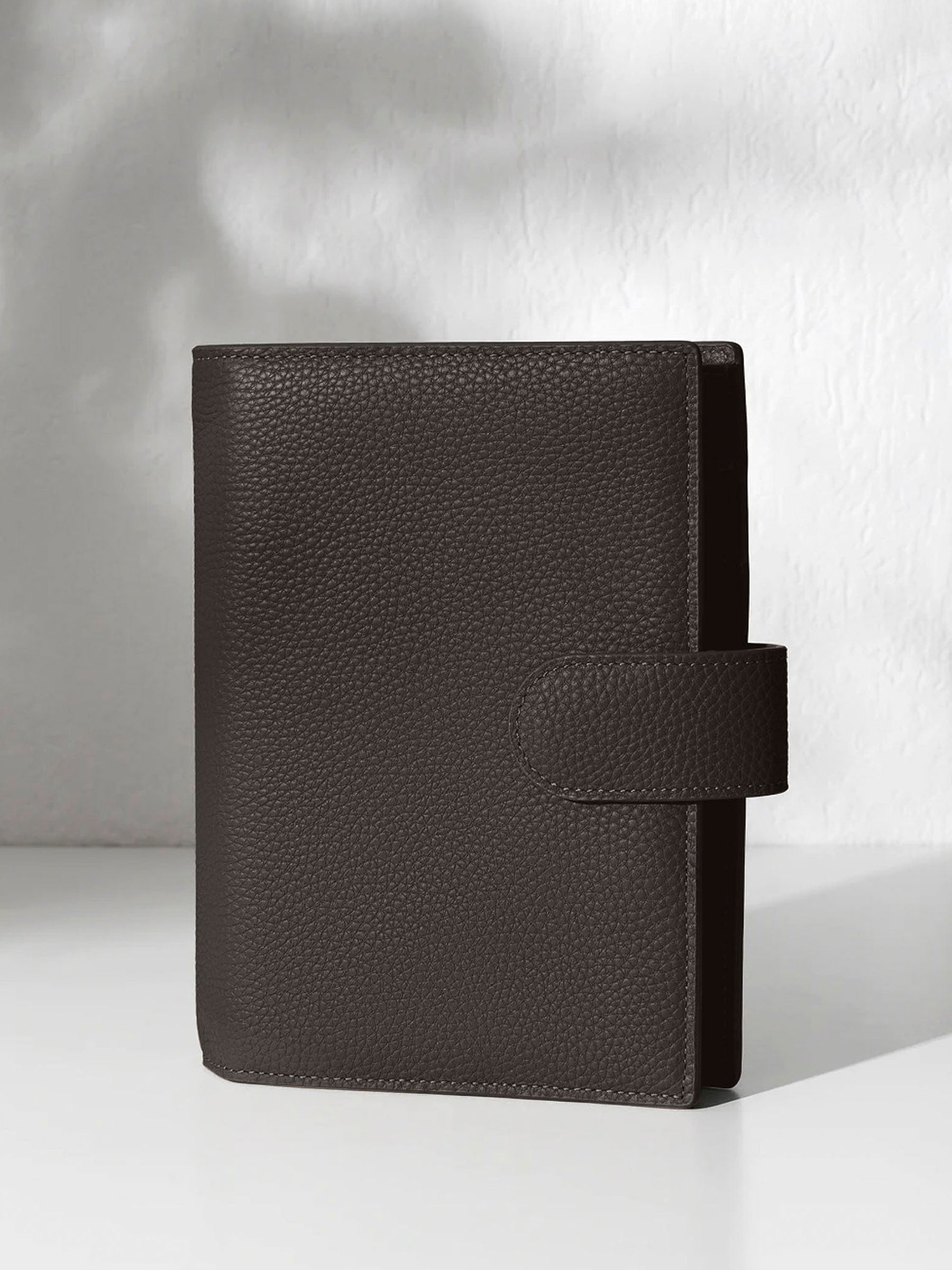 A closed cafenoir leather planner with a closure displayed on an off-white background.