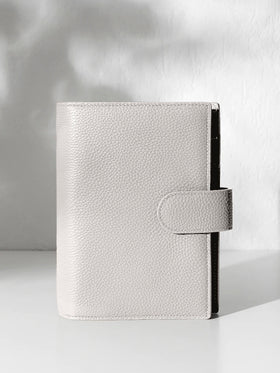 A closed ash leather planner with a closure displayed against a shadowed background.