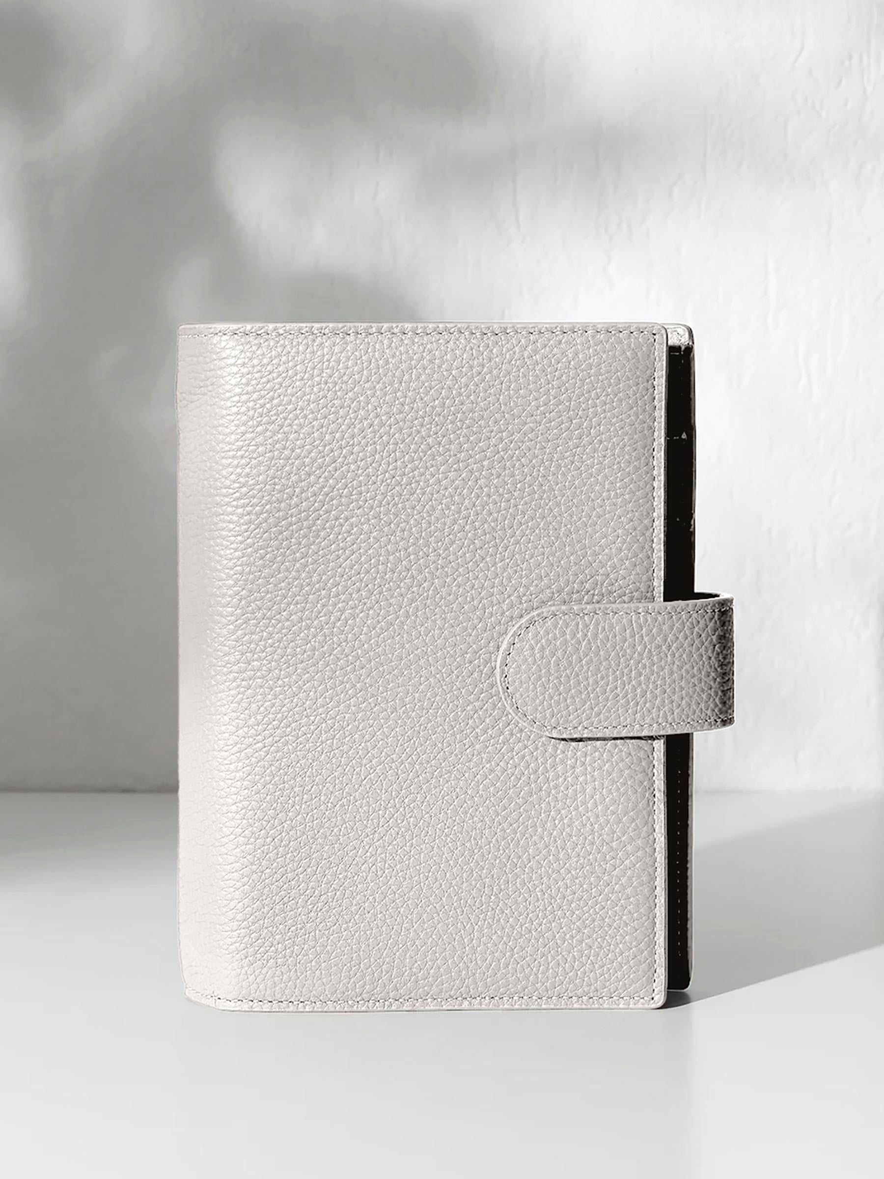 A closed ash leather planner with a closure displayed against a shadowed background.