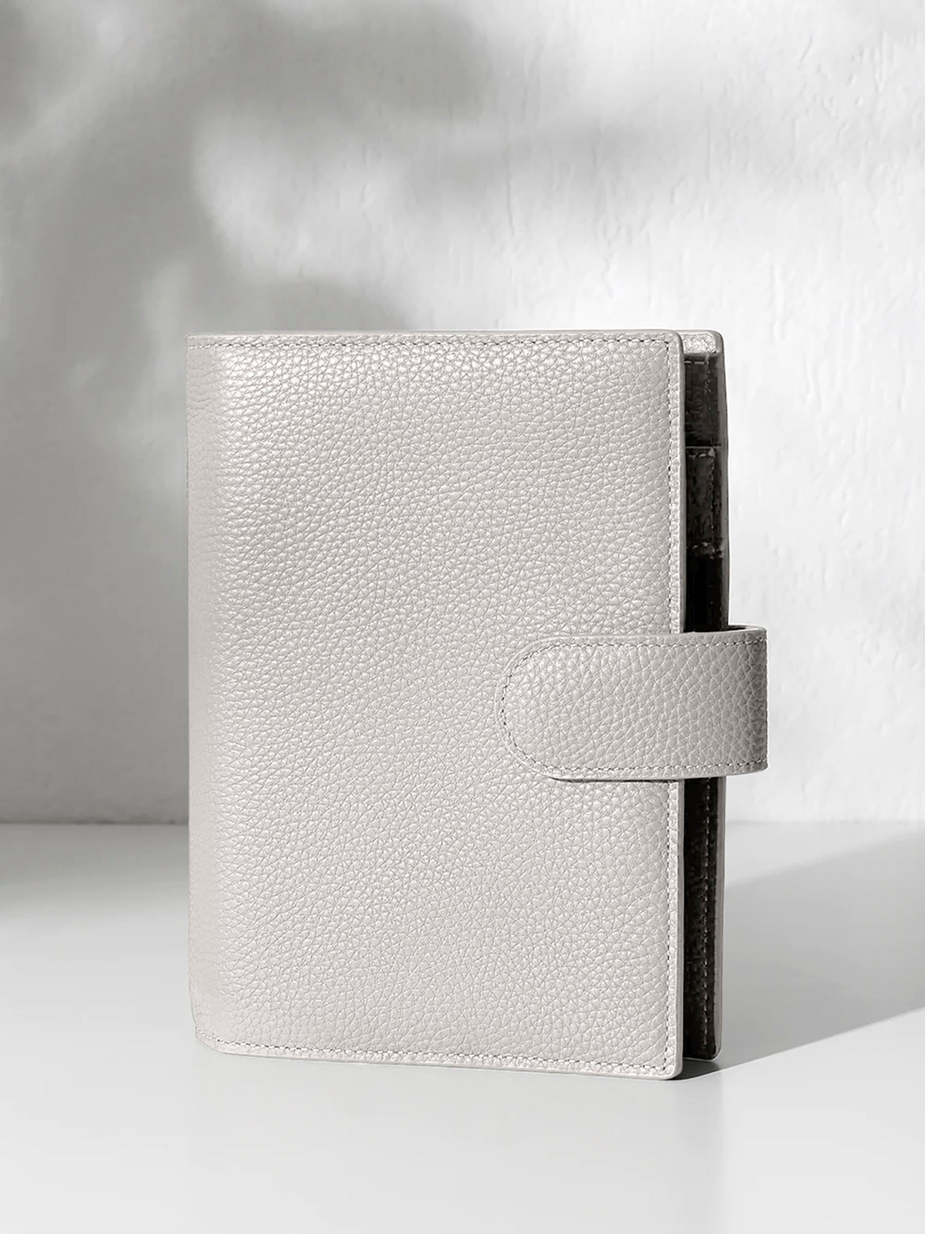 A closed ash leather planner with a closure displayed against a shadowed background.