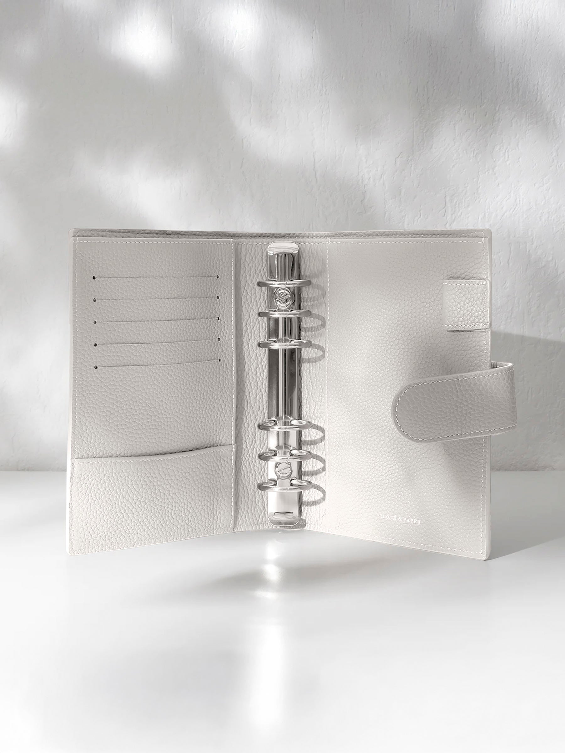 Ash leather agenda displayed against a shadowed background. It is opened to display the silver hardware and company foil stamp.