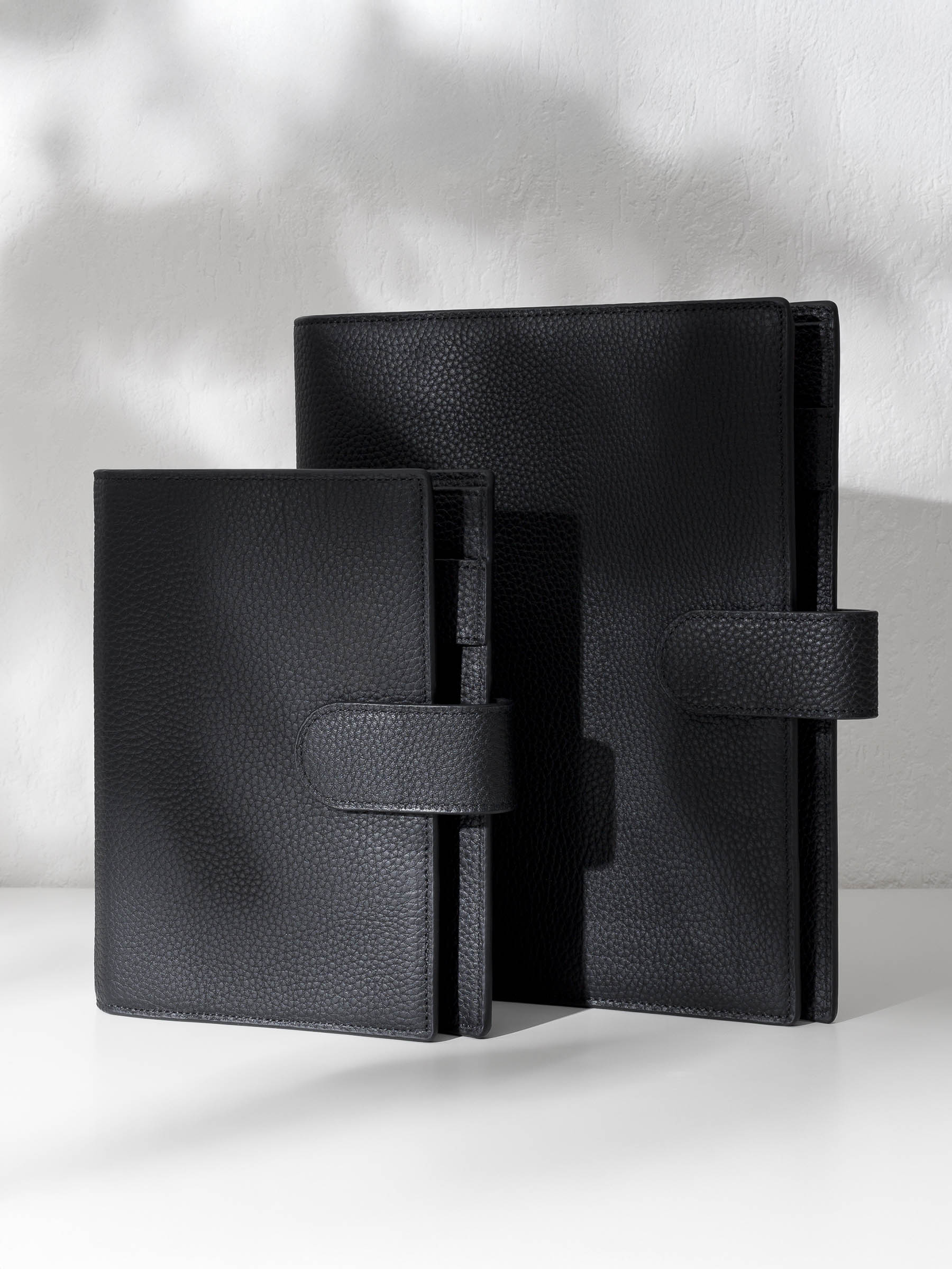 Two black leather agendas displayed against a shadowed background.