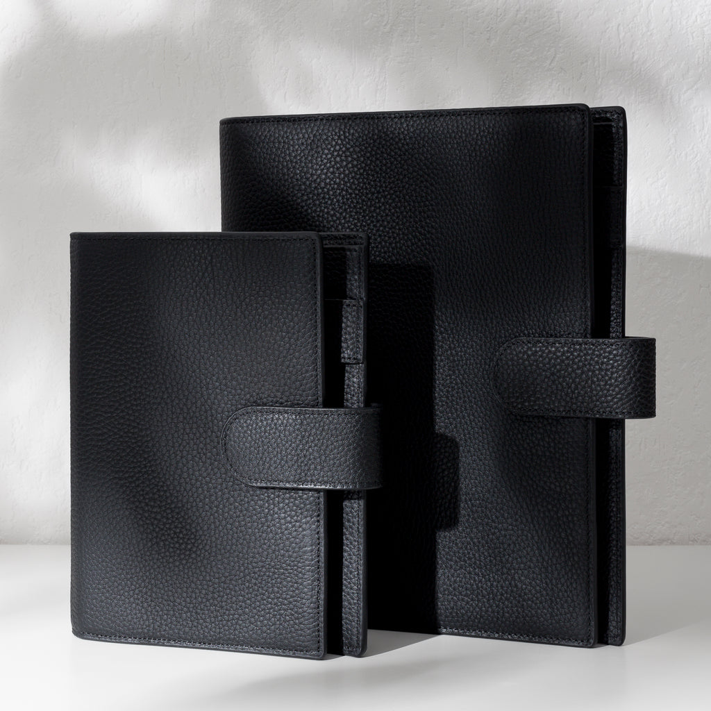 Two black leather agendas displayed on an off-white background.