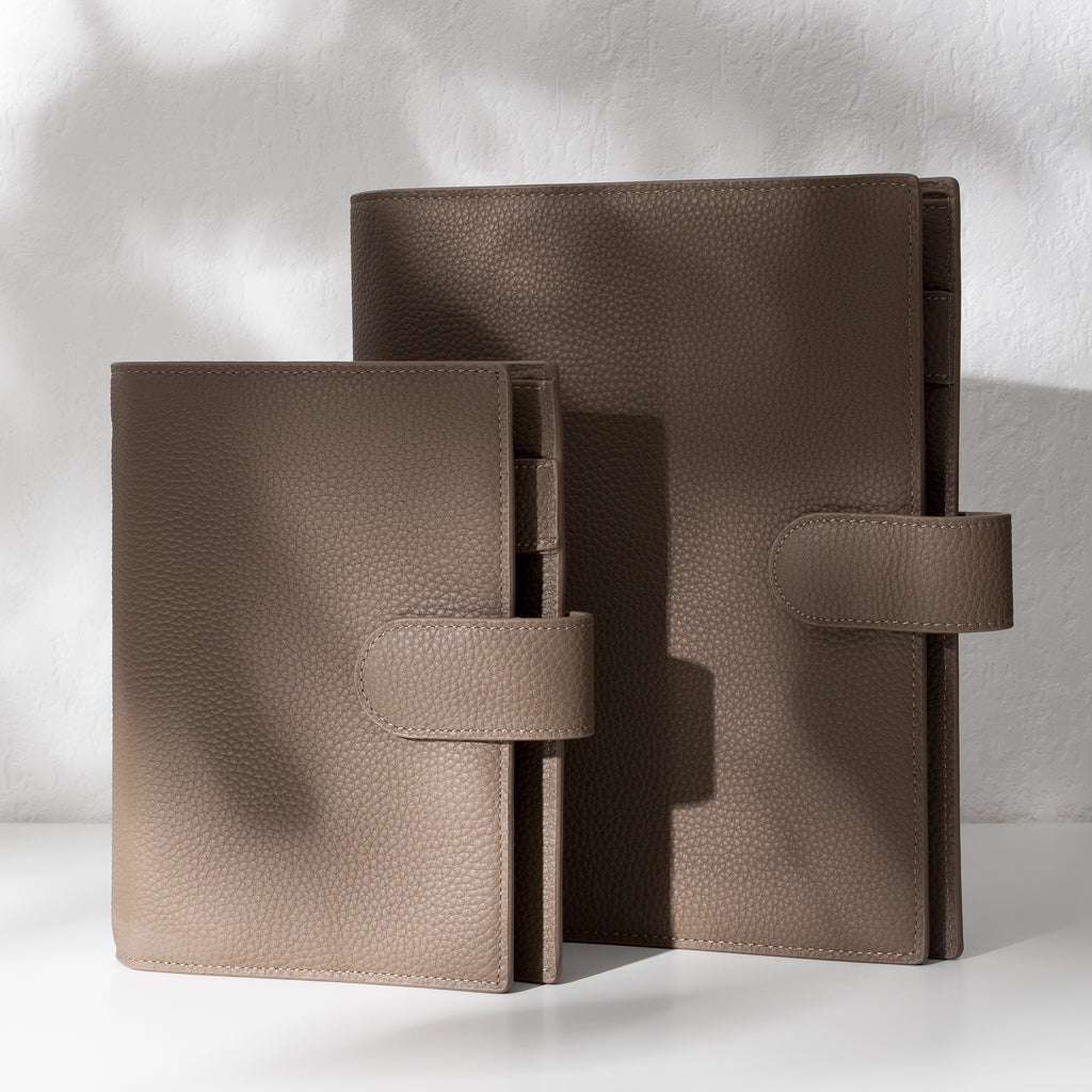 Two brown leather agendas displayed on an off-white background.