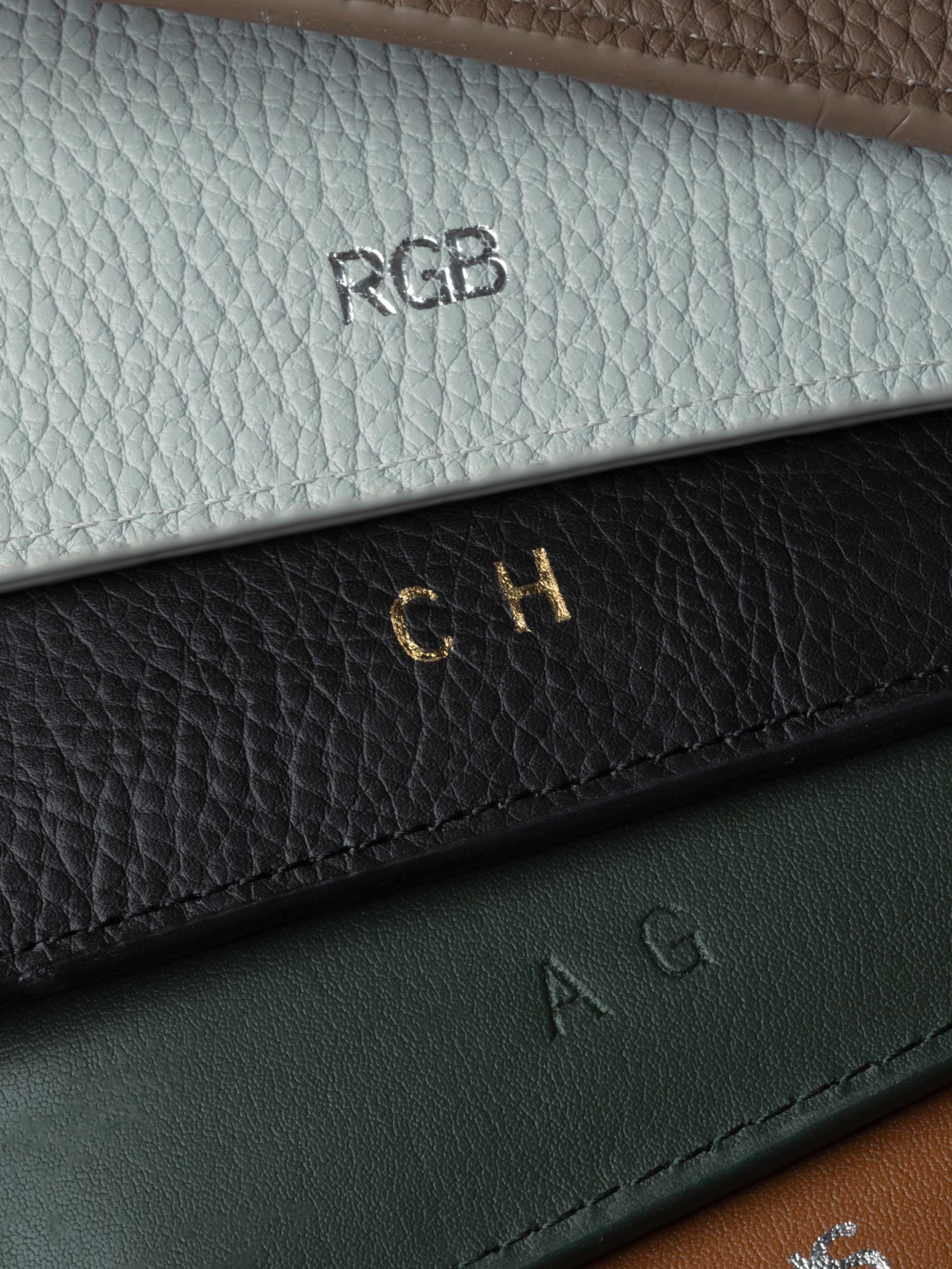 Close-up of the inside bottom edges of leather folio covers with initials debossed in Silver Foil, Gold Foil, and Colorless.