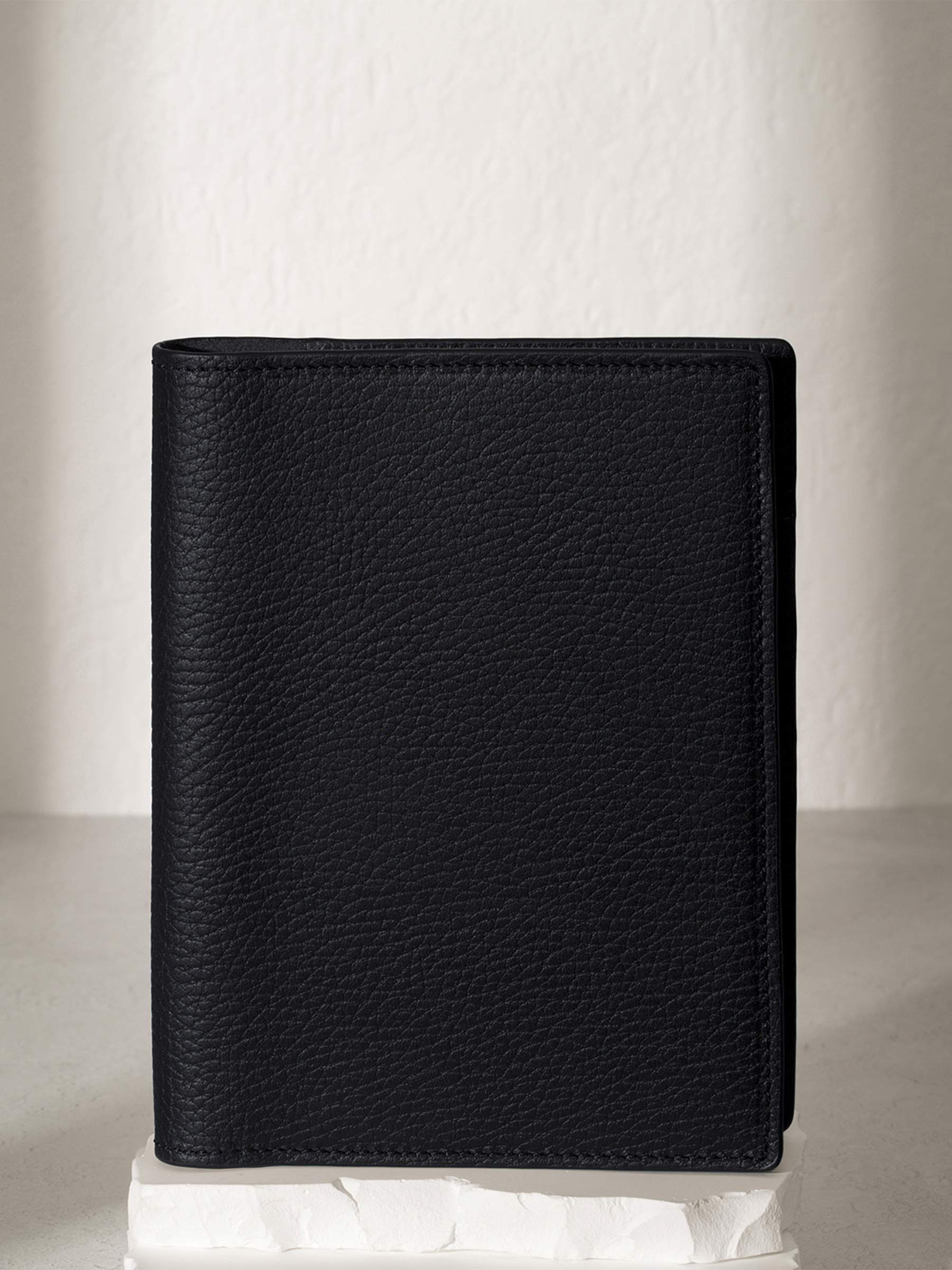 Heirloom Leather Folio, CP Petite, Cloth and Paper. Padrillo folio displayed on a white stone pedestal. The background is a natural textured off-white material, and a spotlight behind the folio highlights its placement.