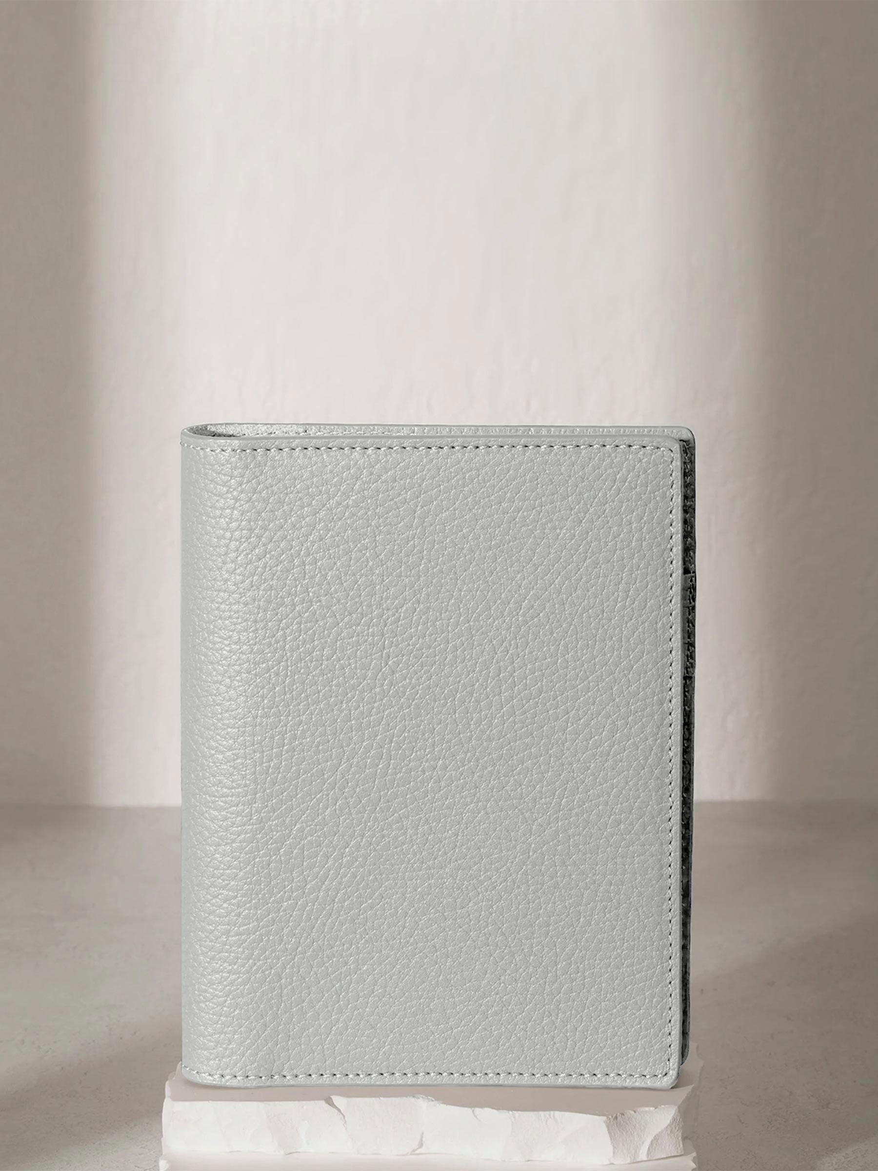 CP Petite Veleta folio displayed on a white stone pedestal. The background is a natural textured off-white material, and a spotlight behind the folio highlights its placement.