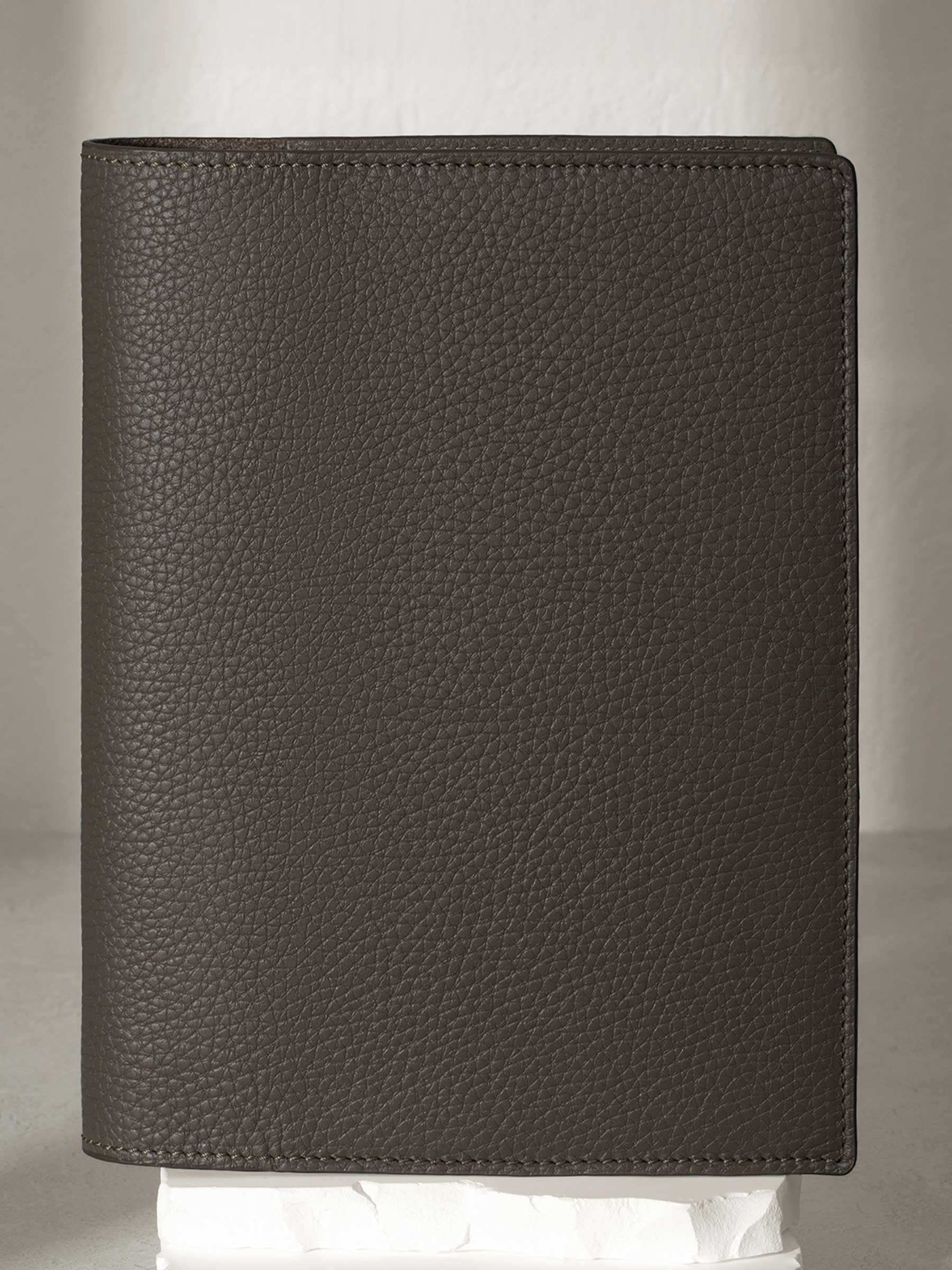 Large Leon folio displayed on a white stone pedestal. The background is a natural textured off-white material, and a spotlight behind the folio highlights its placement.