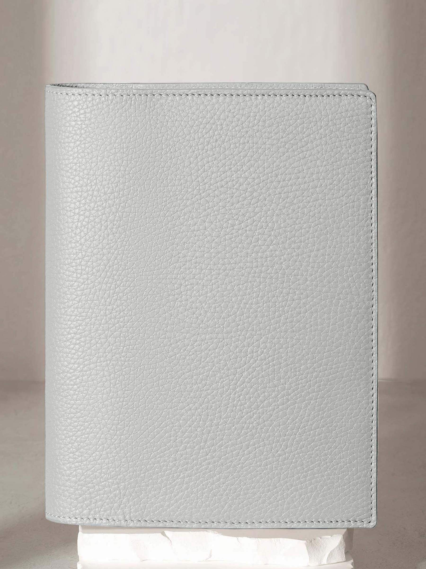 Veleta folio displayed on a white stone pedestal. The background is a natural textured off-white material, and a spotlight behind the folio highlights its placement.