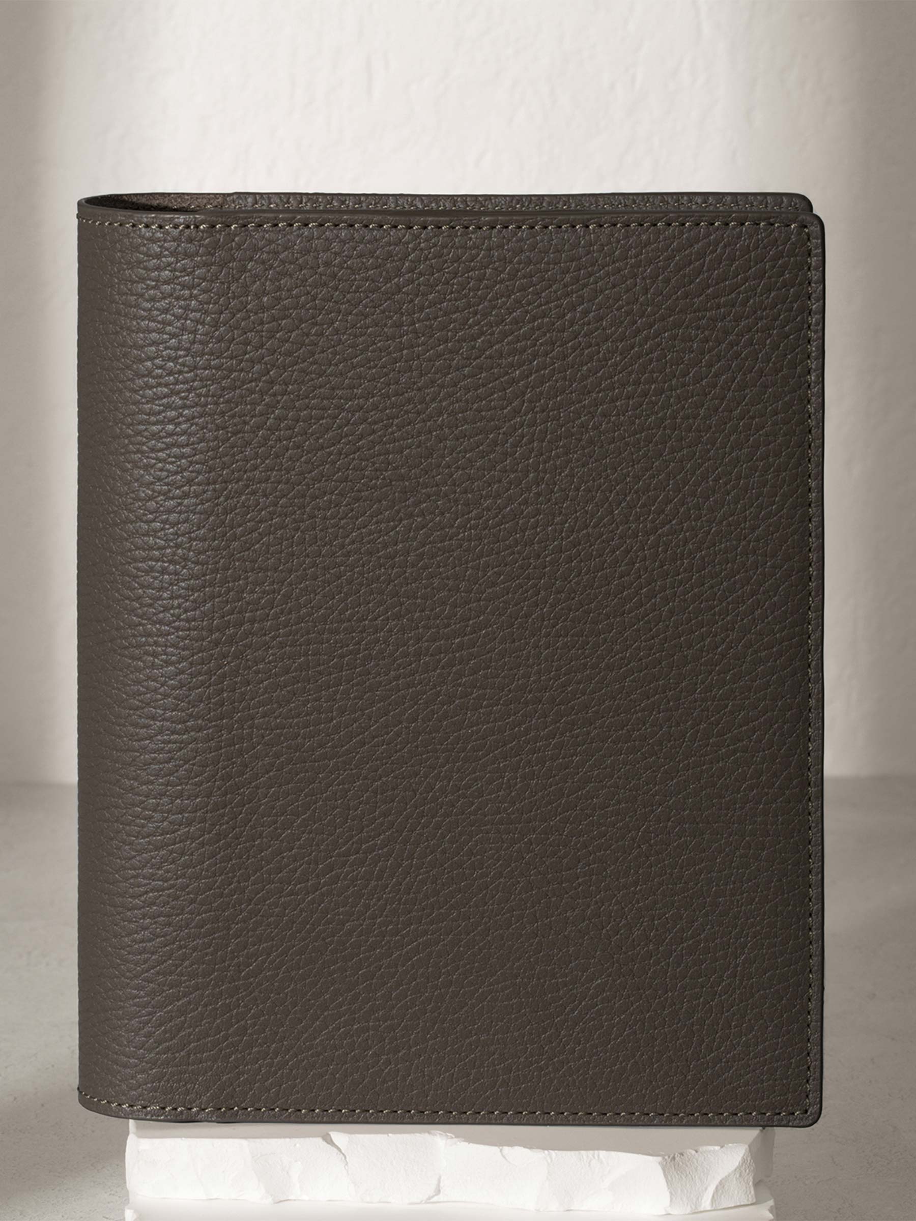 Small Leon folio displayed on a white stone pedestal. The background is a natural textured off-white material, and a spotlight behind the folio highlights its placement.