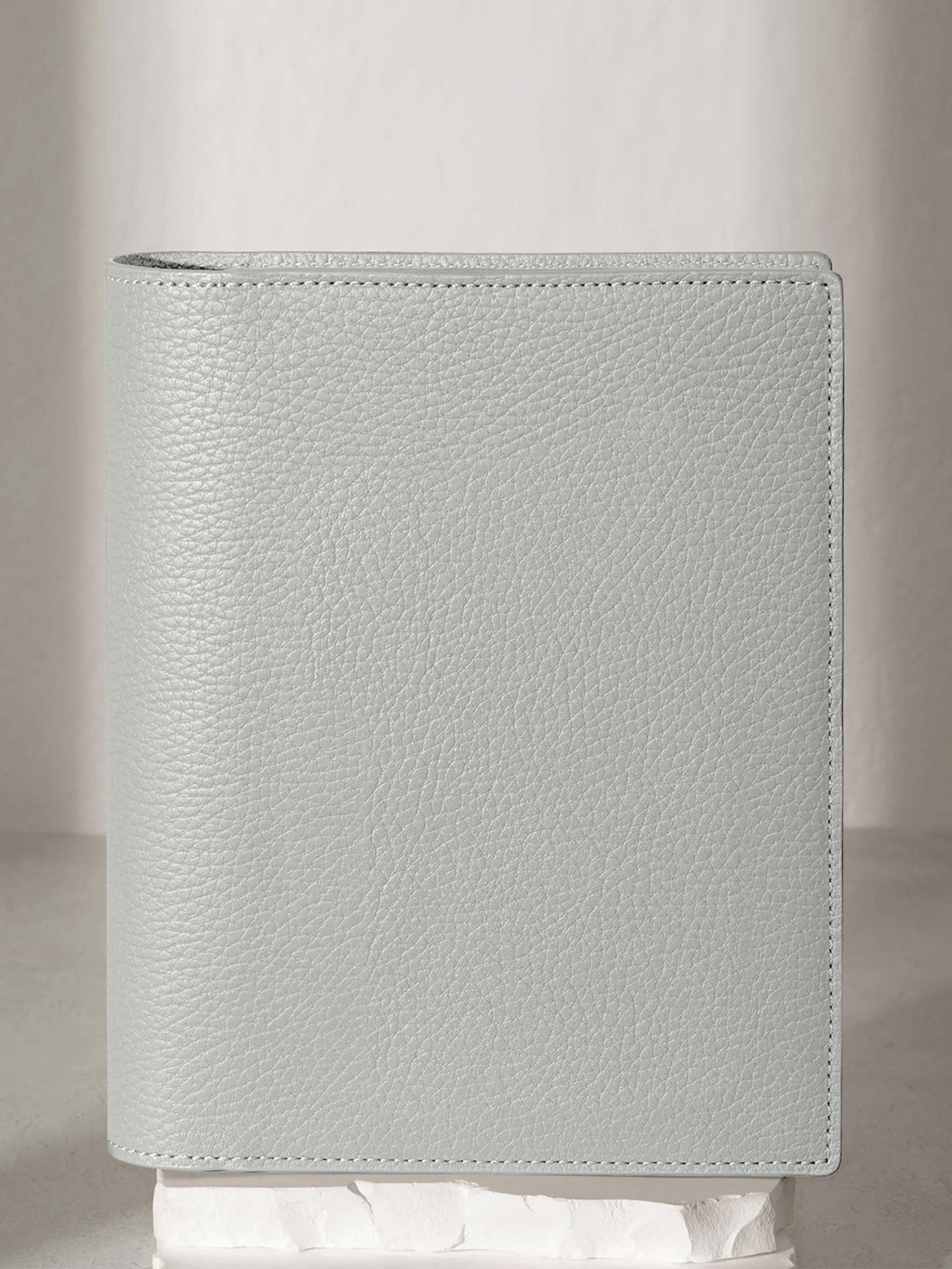 Heirloom Leather Folio, Small, Cloth and Paper. Veleta folio displayed on a white stone pedestal. The background is a natural textured off-white material, and a spotlight behind the folio highlights its placement.
