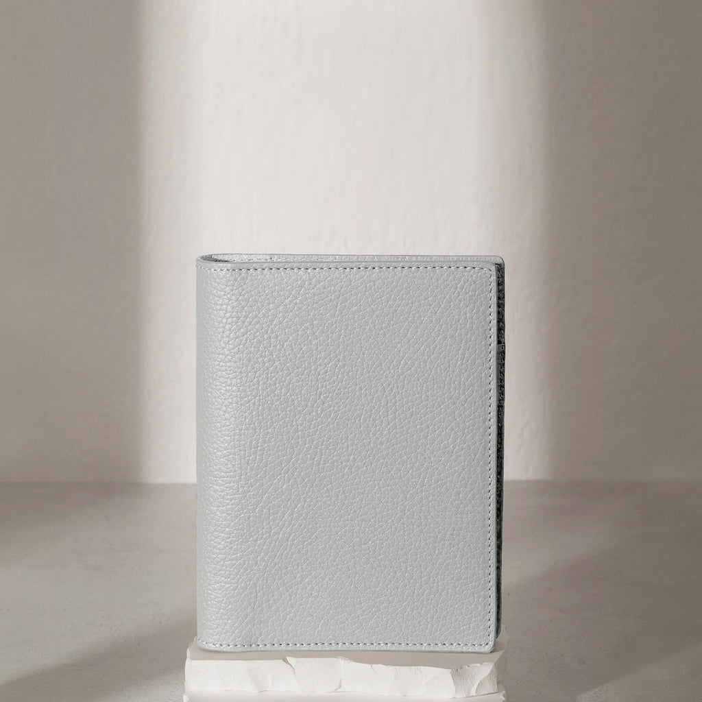 CP Petite Veleta folio displayed on a white stone pedestal. The background is a natural textured off-white material, and a spotlight behind the folio highlights its placement.
