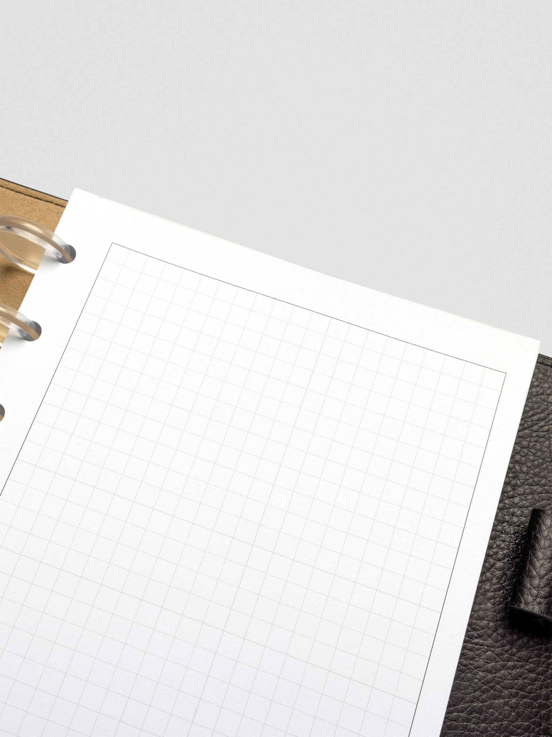 A close-up of the upper right corner of a grid paper insert, highlighting the fine grid pattern and subtle border, resting against black leather planner cover.