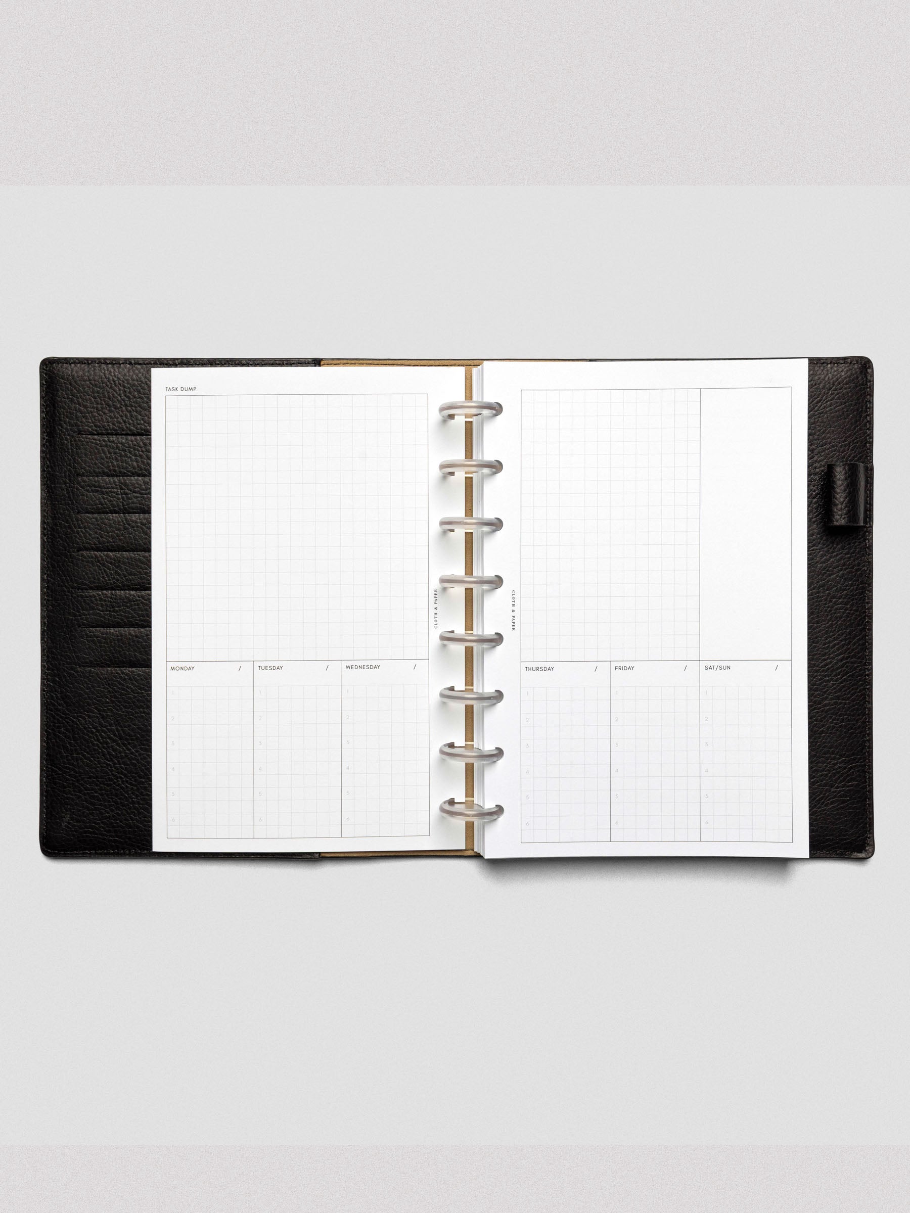 A weekly planner spread featuring a large "Task Dump" section at the top and segmented days of the week below, with six numbered grid slots for each day. Bound in a black leather discbound planner.
