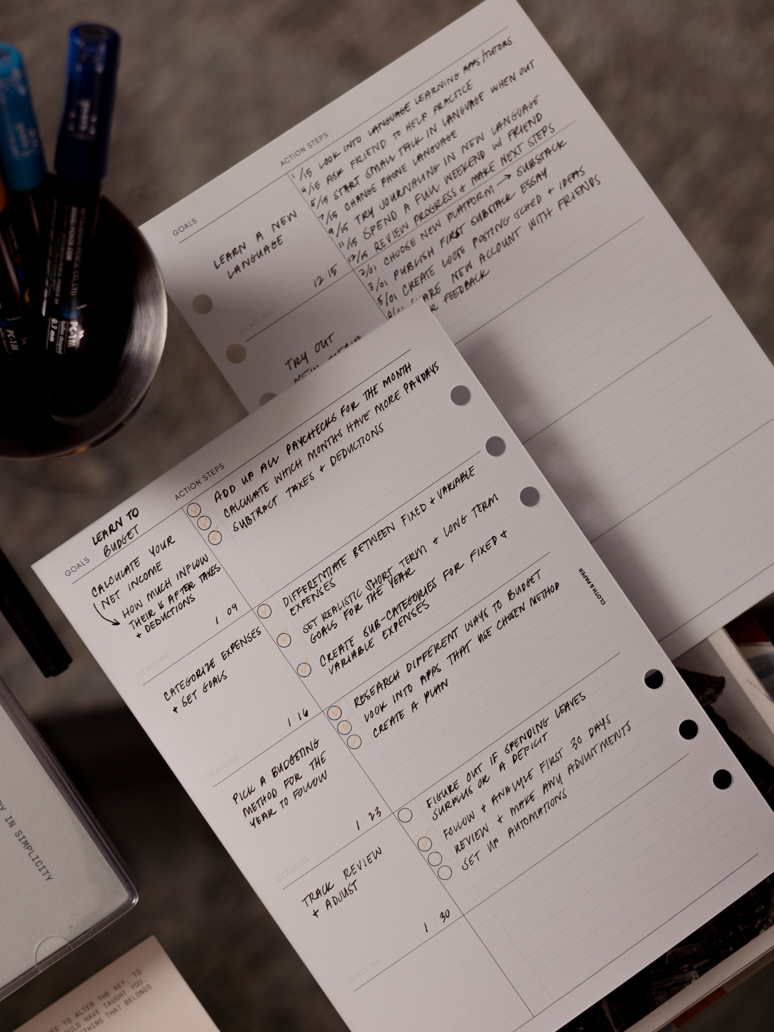 Goal Tracking Planner Inserts | 3rd Edition shown filled with handwritten notes and bullet points resting on a glass coffee table.