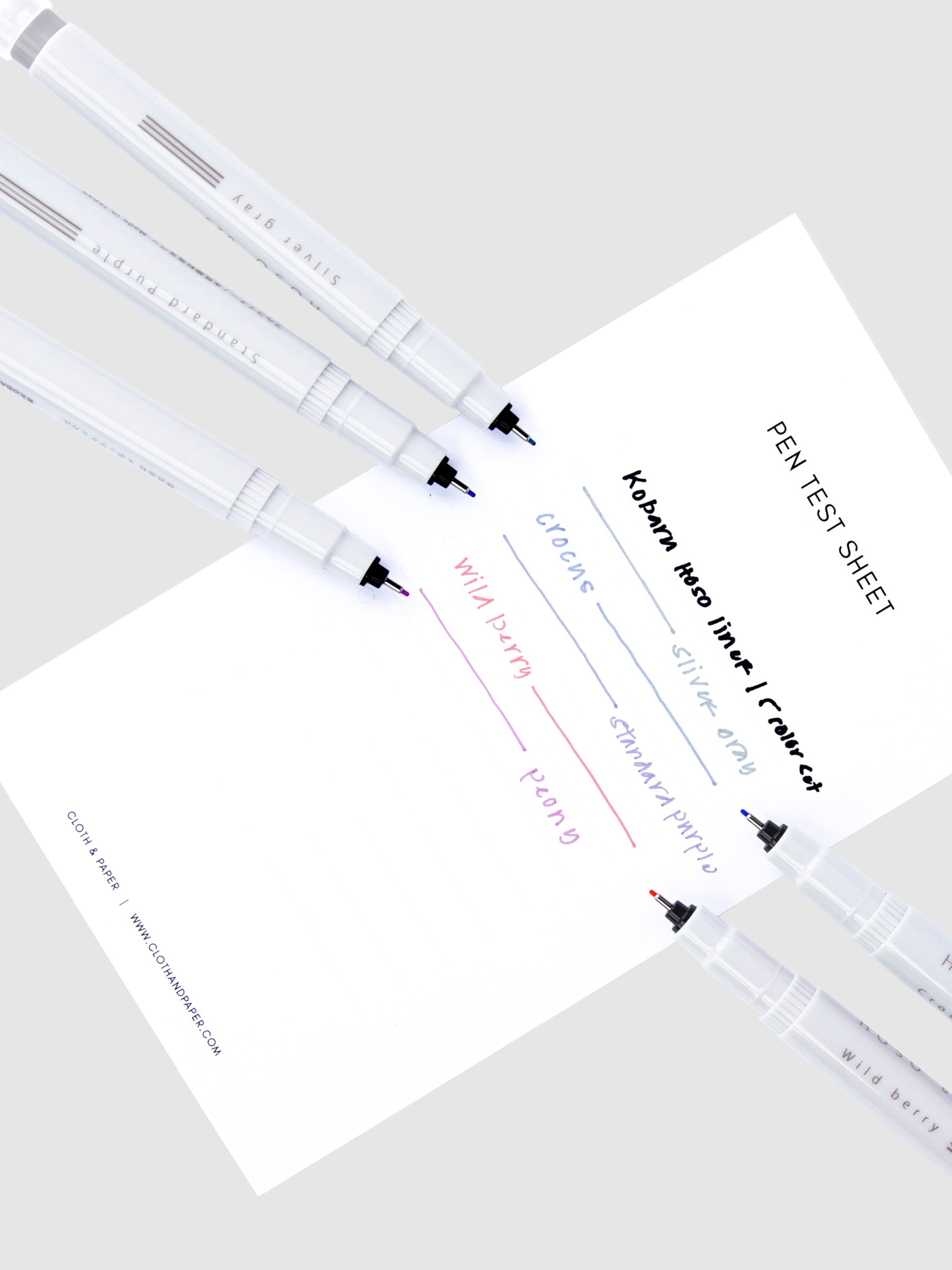 Pen test sheet showing examples of Silver Gray, Crocus, Standard Purple, Wild Berry, and Peony ink. All five pens rest with nibs exposed on top of the pen test sheet. 