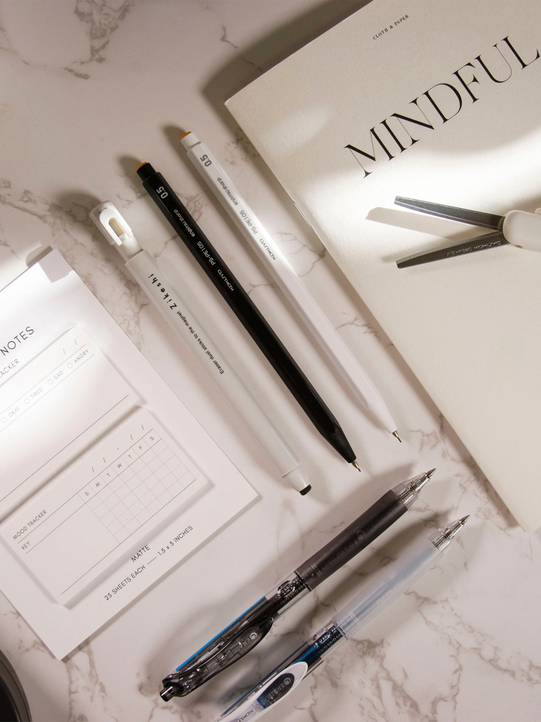 Kokuyo Enpitsu Sharp Mechanical Pencil. 0.5, Black, Cloth and Paper. Mechanical pencil styled with eraser, sticky notes, pens, scissors, and a notebook, all on a marble surface.