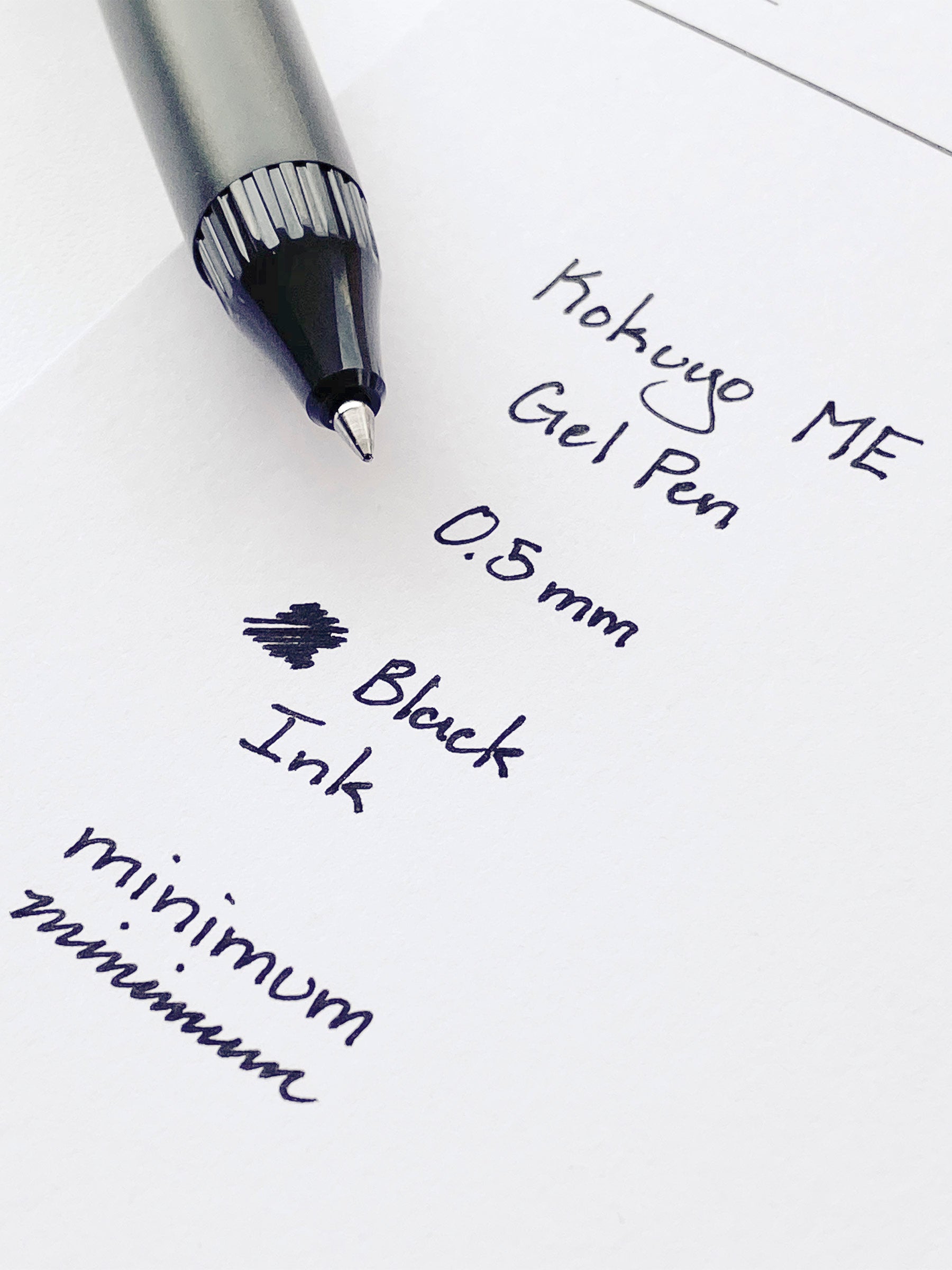 Kokuyo ME Gel Pen, Grayish Black, Cloth and Paper. Pen resting on pen test sheet displaying writing sample.