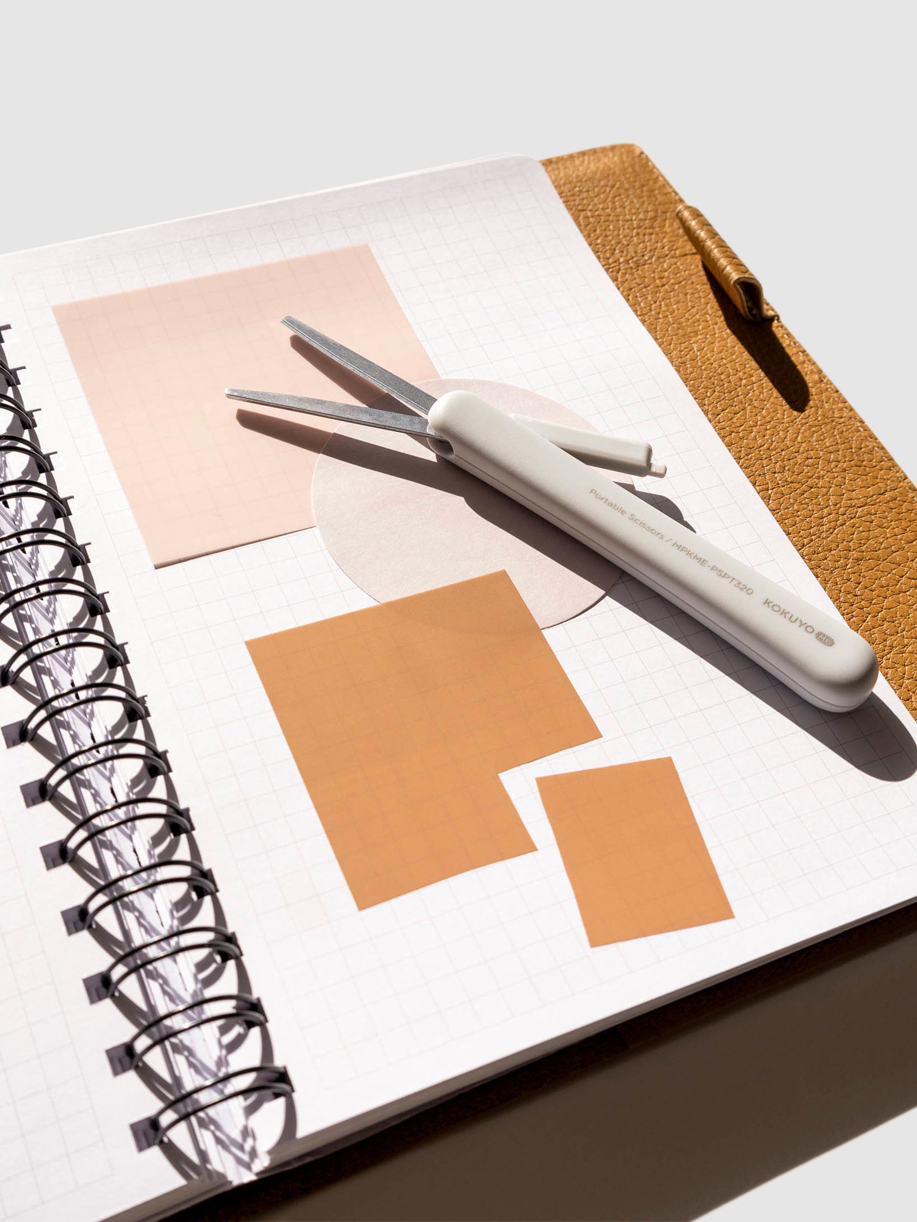 Grayish Ice scissors displayed in a notebook inside a brown leather folio. Several transparent sticky notes are layered on each other, with one being cut into a smaller square.