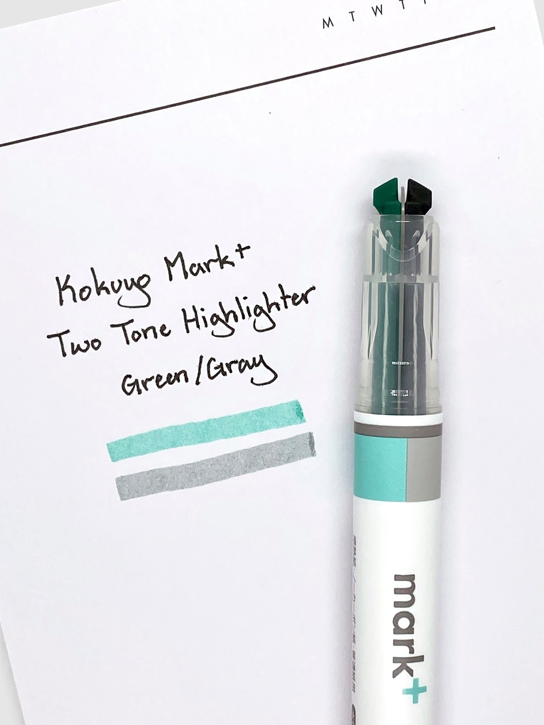 Highlighter resting on a sheet of paper with a writing samples of the two highlighter inks on it.