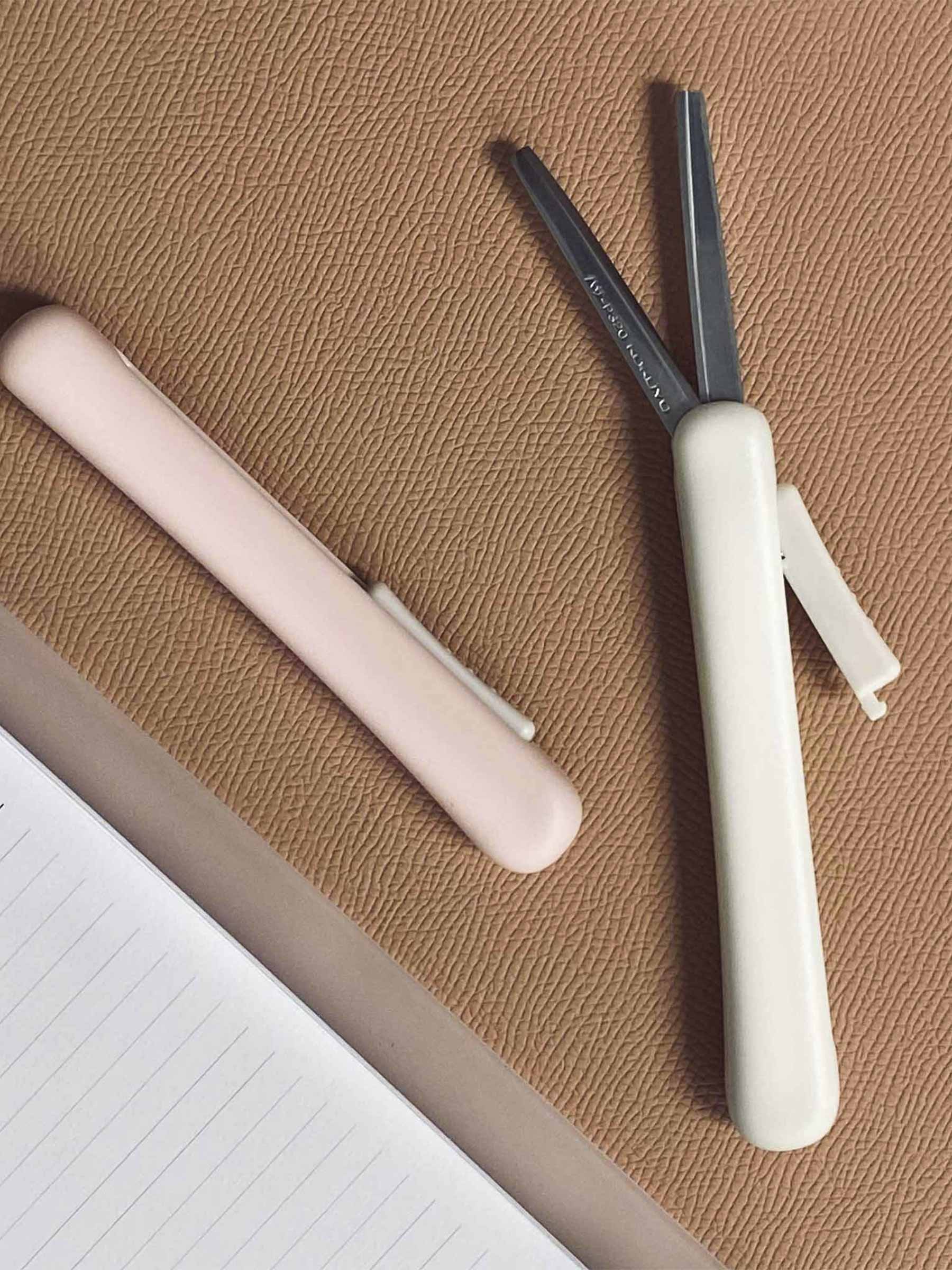 White and Peach scissors on a rust colored surface next to a planner. The white scissors are extended to show the blades.