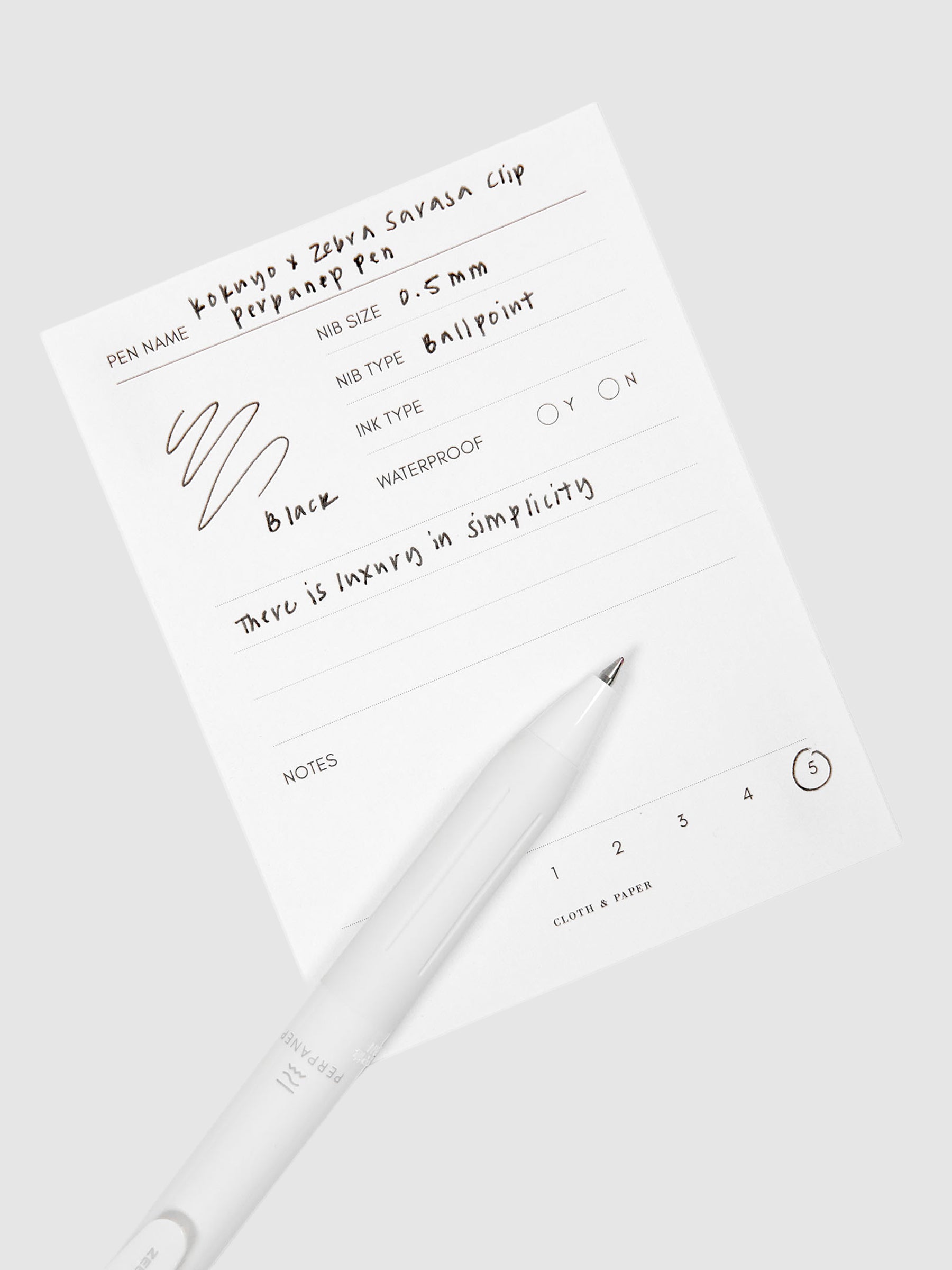 Kokuyo x Zebra Sarasa Clip Perpanep Pen, Cloth and Paper. Pen resting on pen test sheet displaying writing sample.