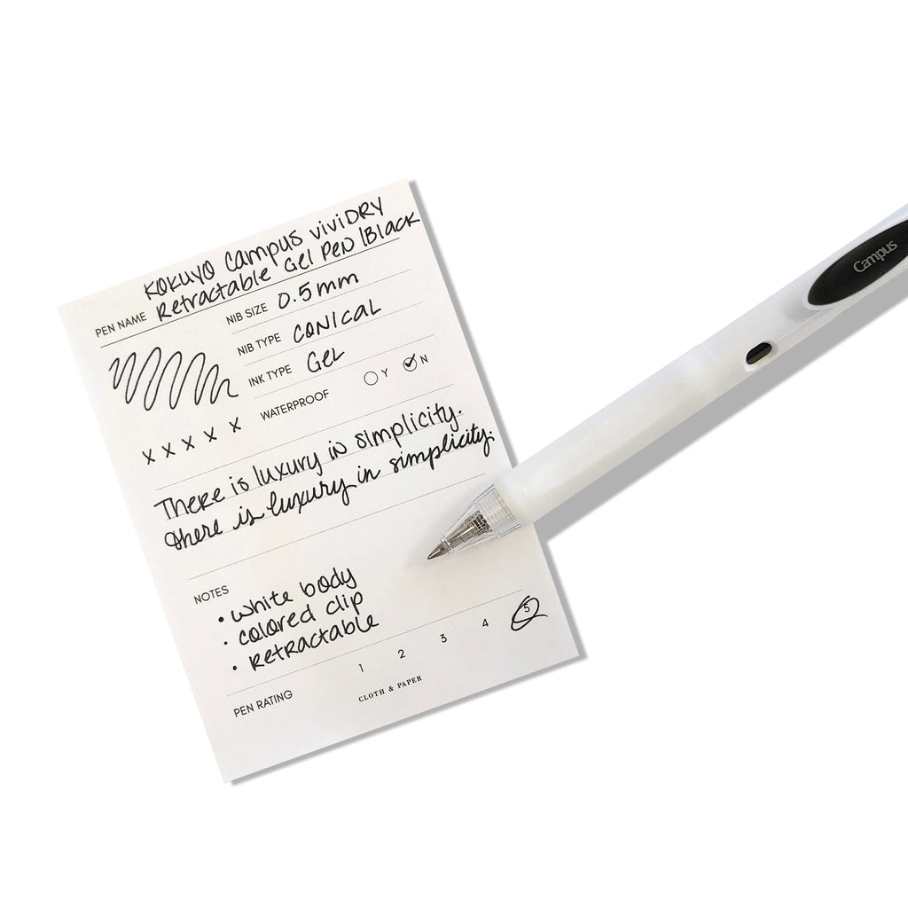 Kokuyo Campus viviDRY Retractable Gel Pen | Black | Cloth & Paper. Pen resting on pen test sheet displaying writing sample.