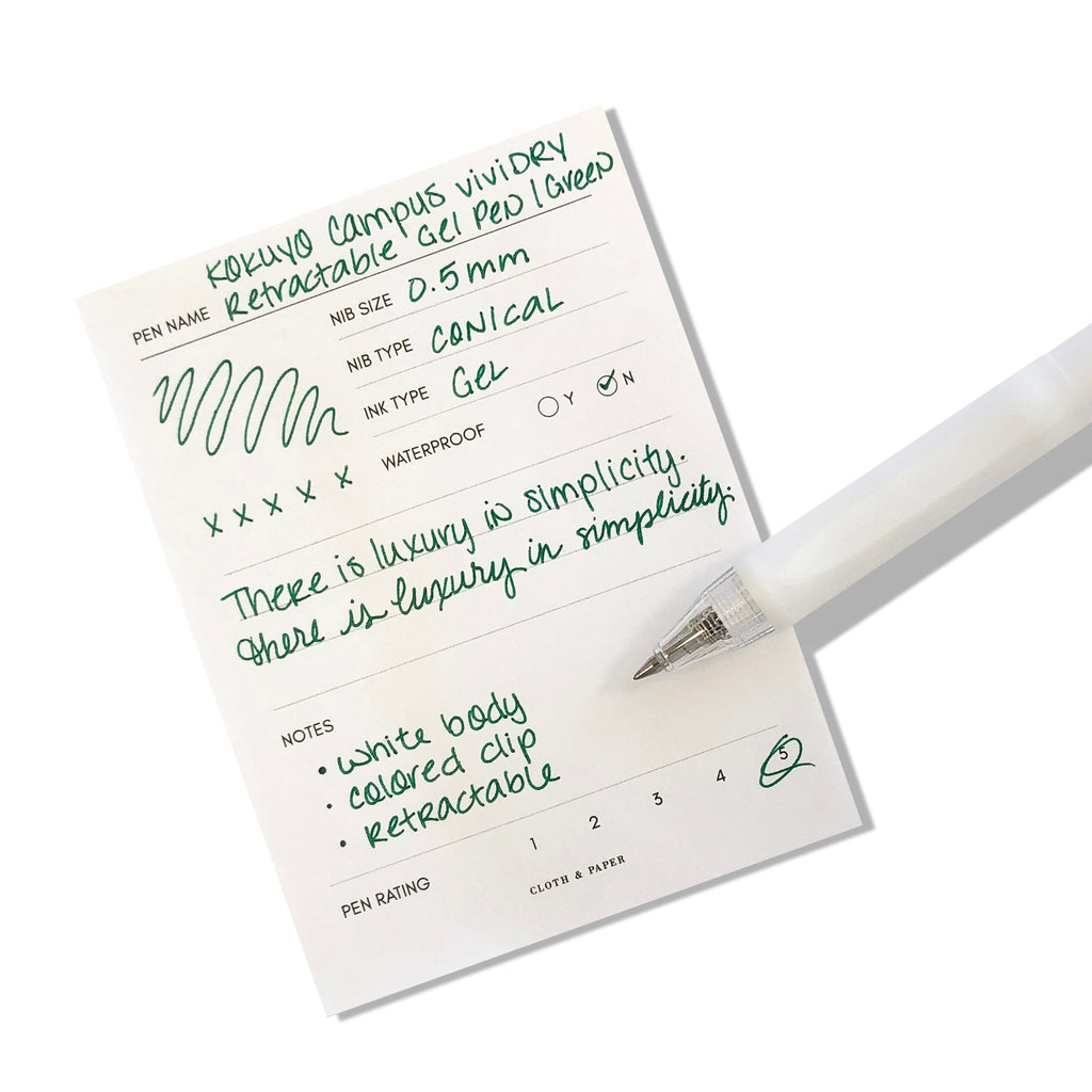 Kokuyo Campus viviDRY Retractable Gel Pen | Green | Cloth & Paper. Pen resting on pen test sheet displaying writing sample.