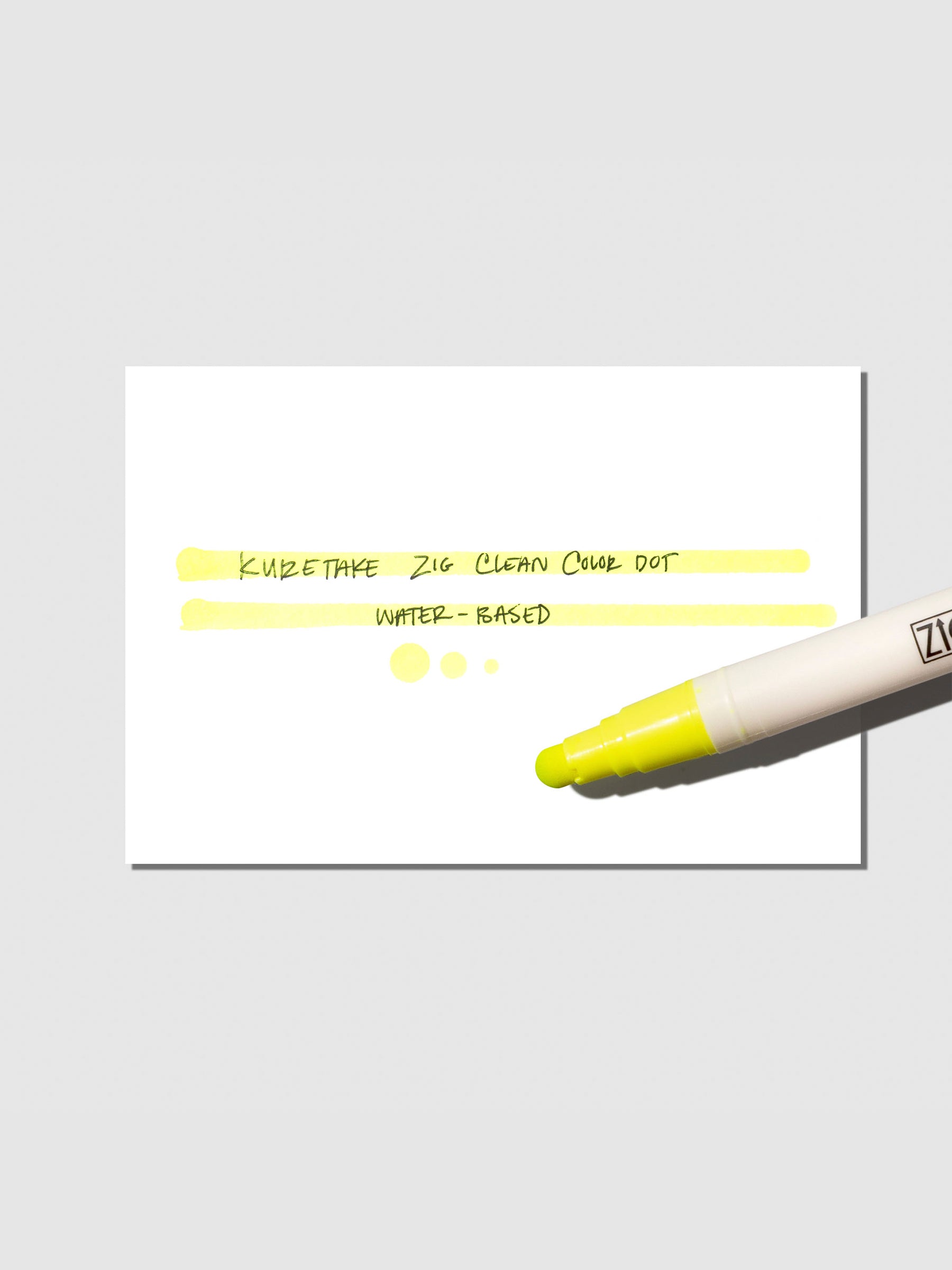 Kuretake Zig Clean Color Dot Marker in Yellow displayed next to a writing sample on a neutral background.