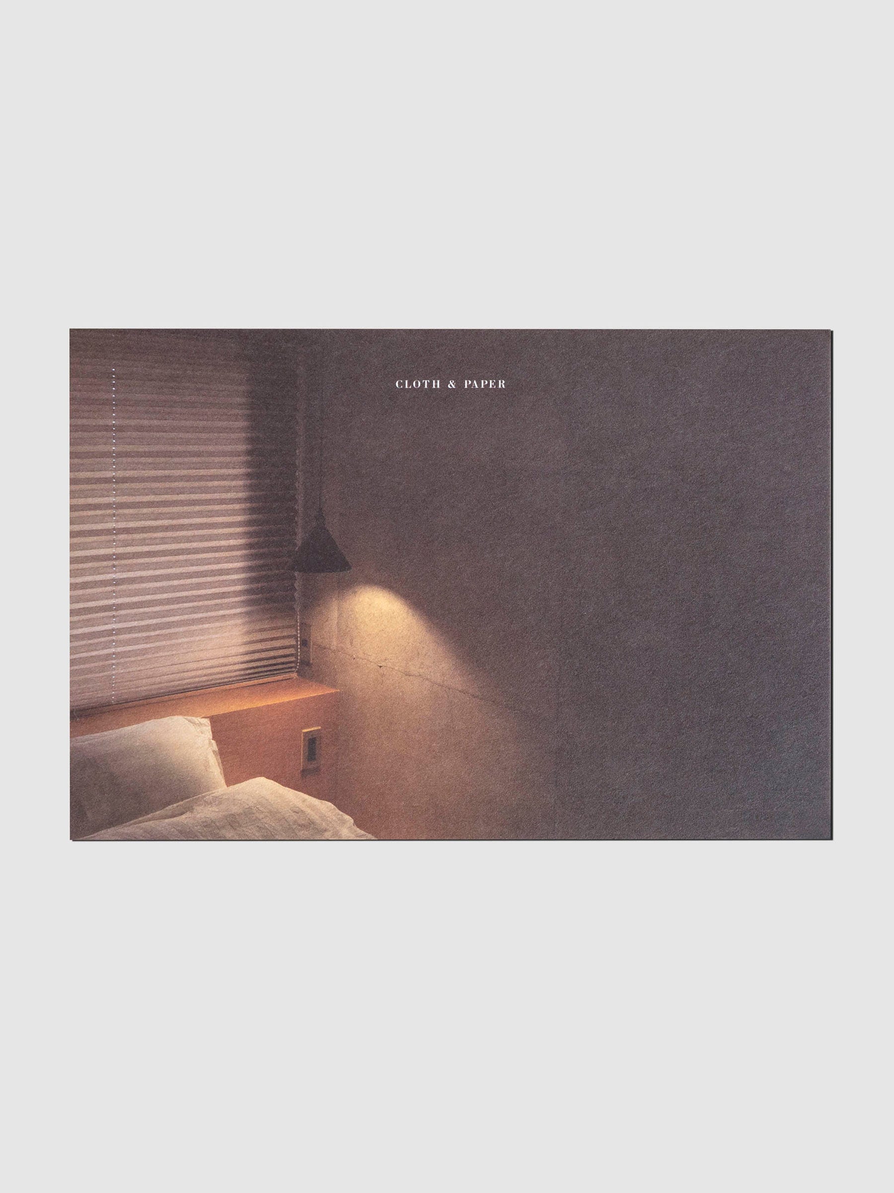 Full color printed postcard, showcase a hotel bed lit warmly by an overhead lamp.