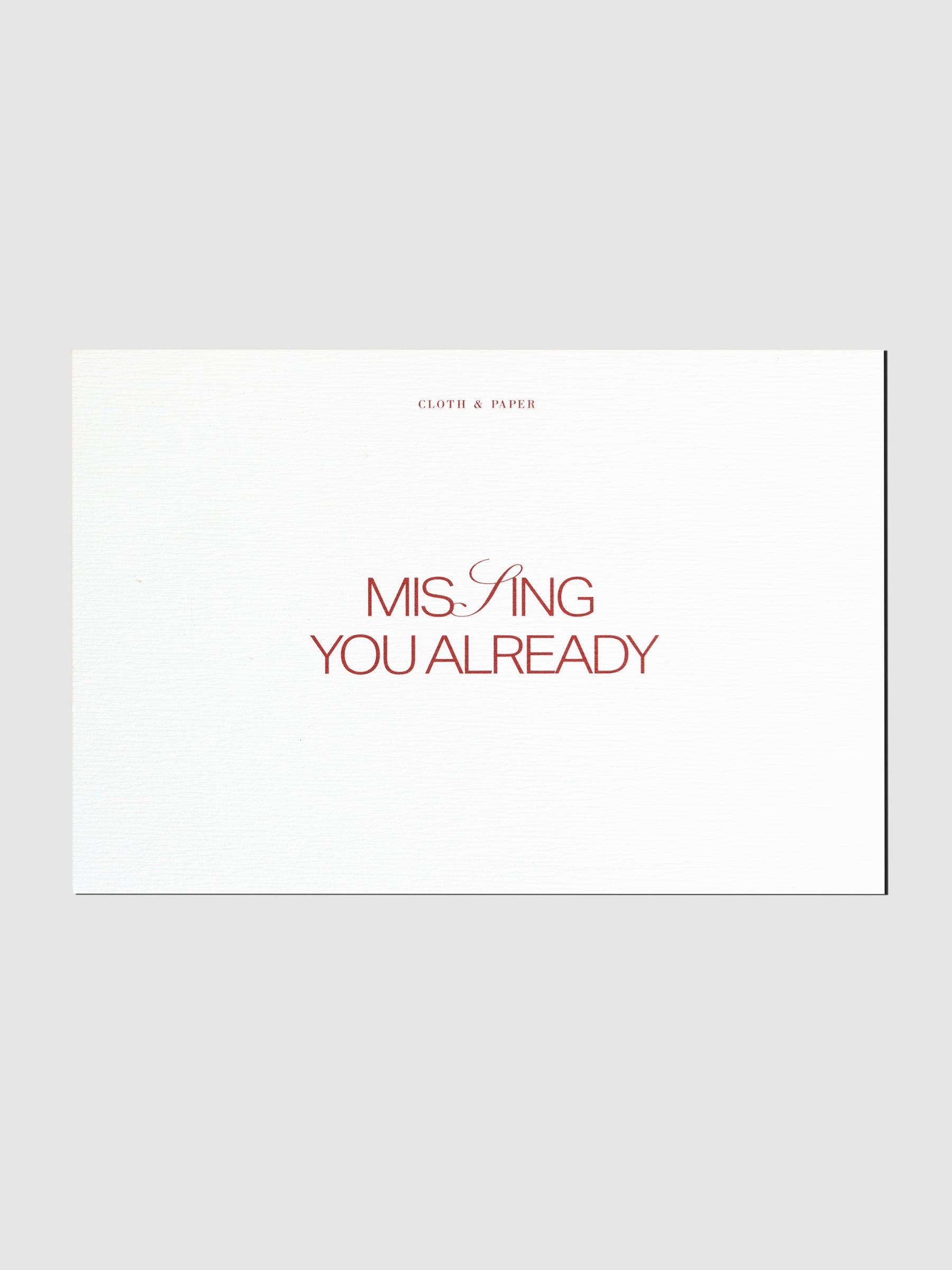 Postcard displayed on a neutral background. Text is printed in red and reads "Missing You Already"