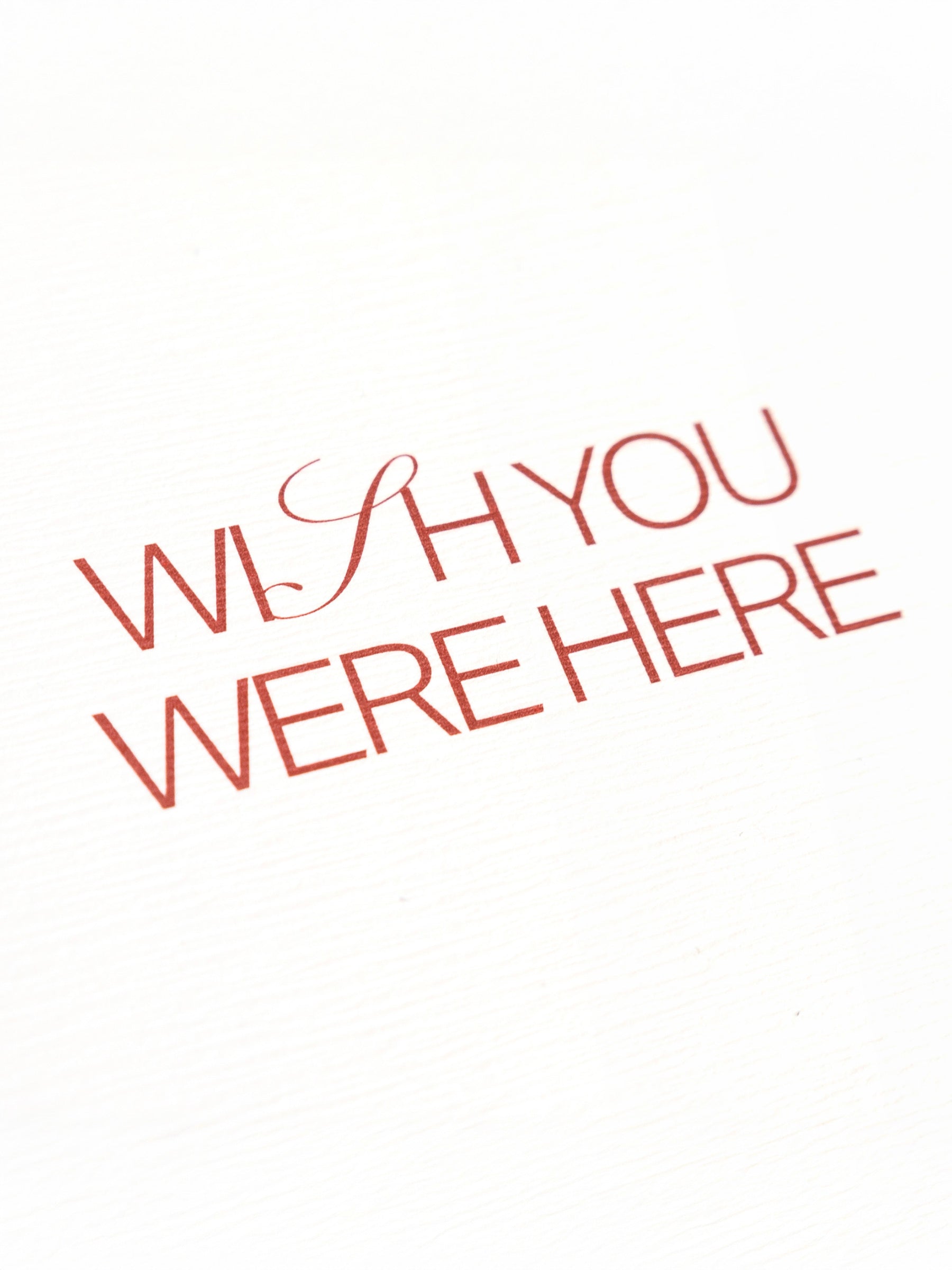 Closeup of red text on a postcard that reads "Wish You Were Here"