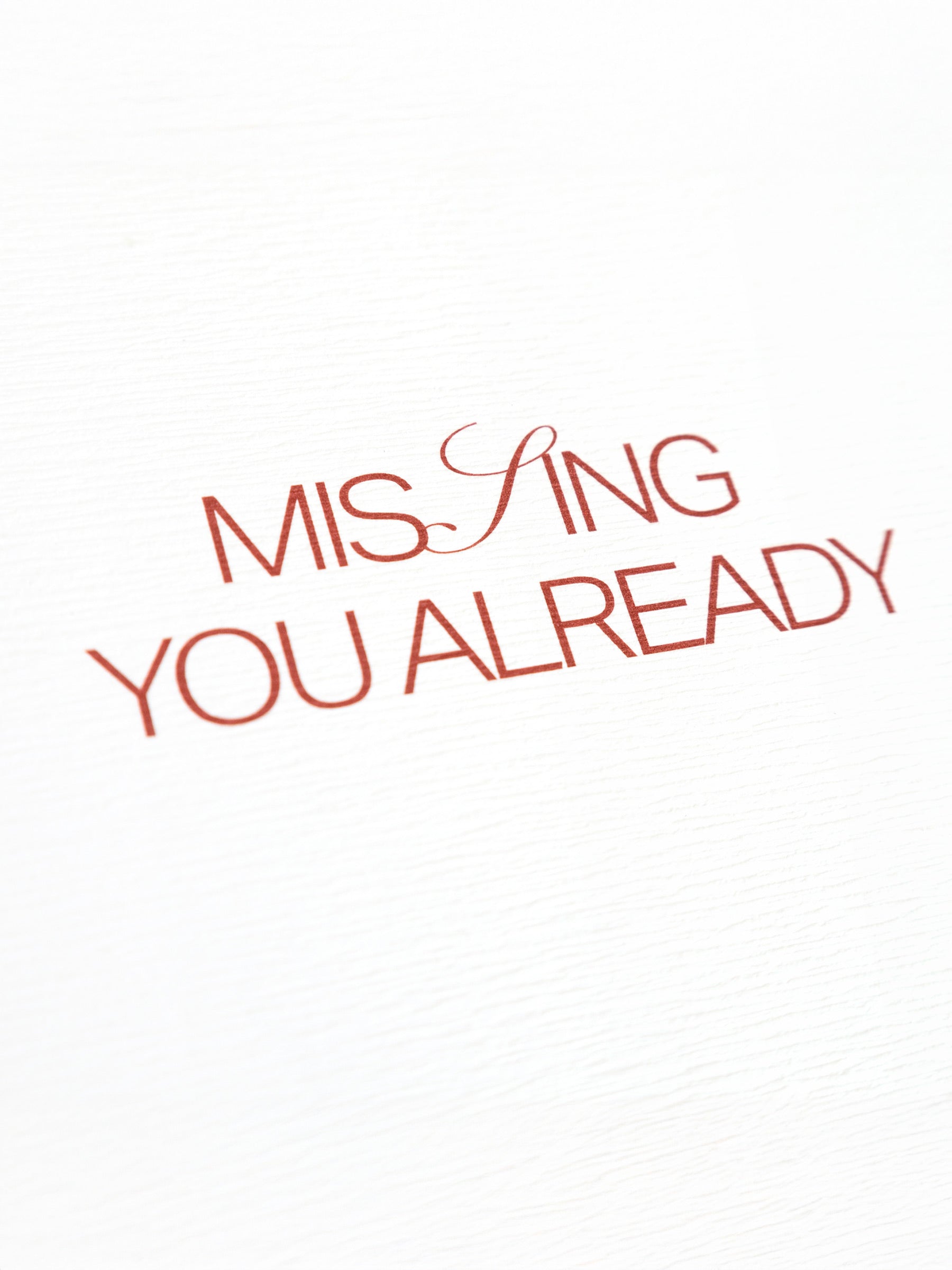 Closeup of red text on a postcard that reads "Missing You Already"