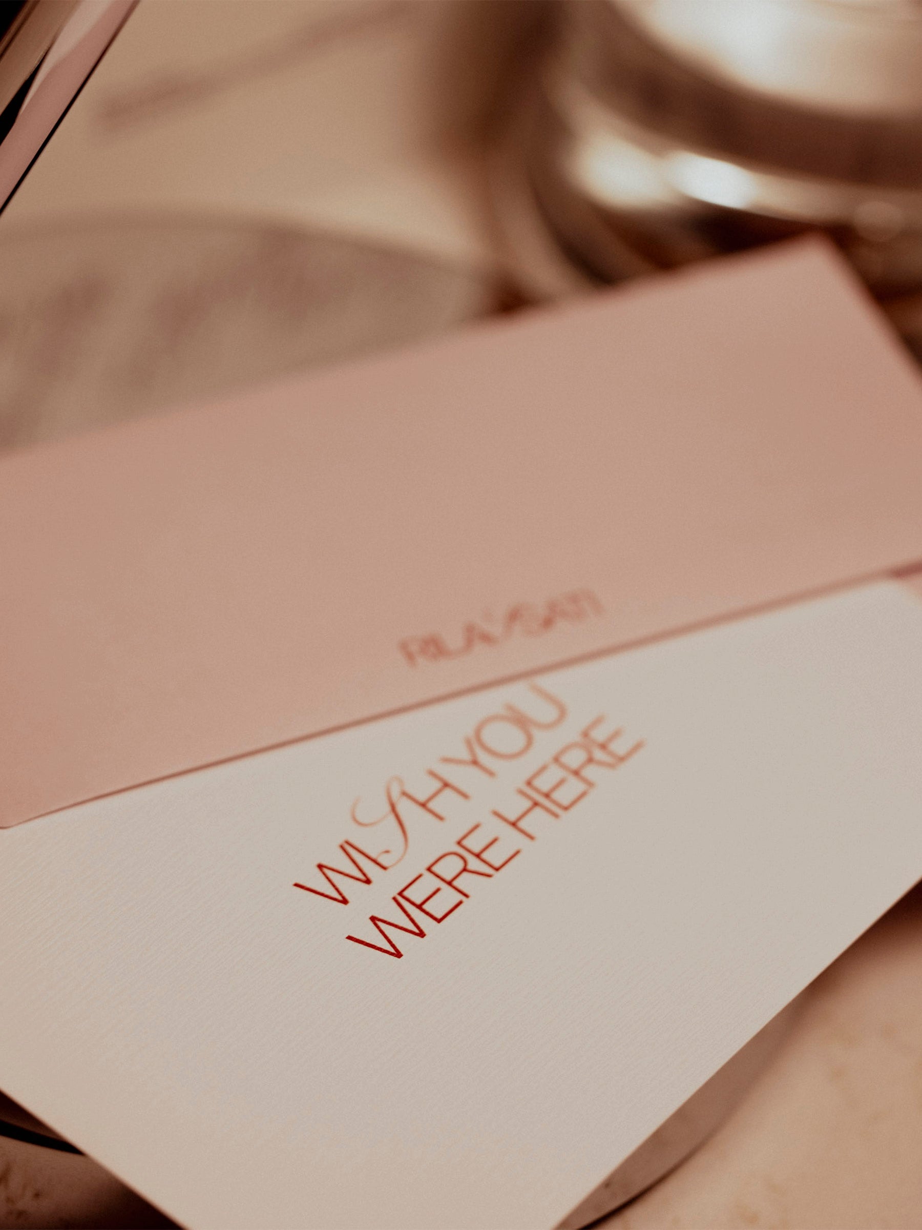 Postcard displayed with envelope on a warmly lit table. They are both resting on a table lamp's base.