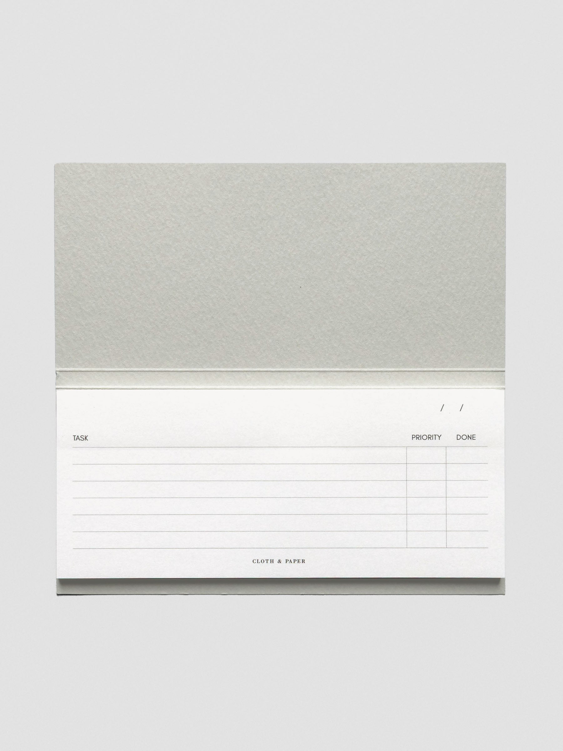 Horizontal view of the notepad fully open, highlighting its landscape layout and structured task, priority, and completion columns with subtle branding at the bottom.