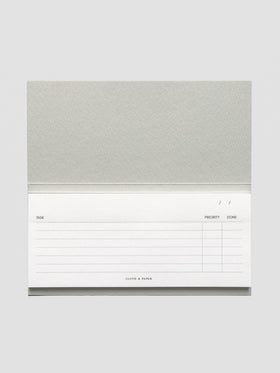 Horizontal view of the notepad fully open, highlighting its landscape layout and structured task, priority, and completion columns with subtle branding at the bottom.