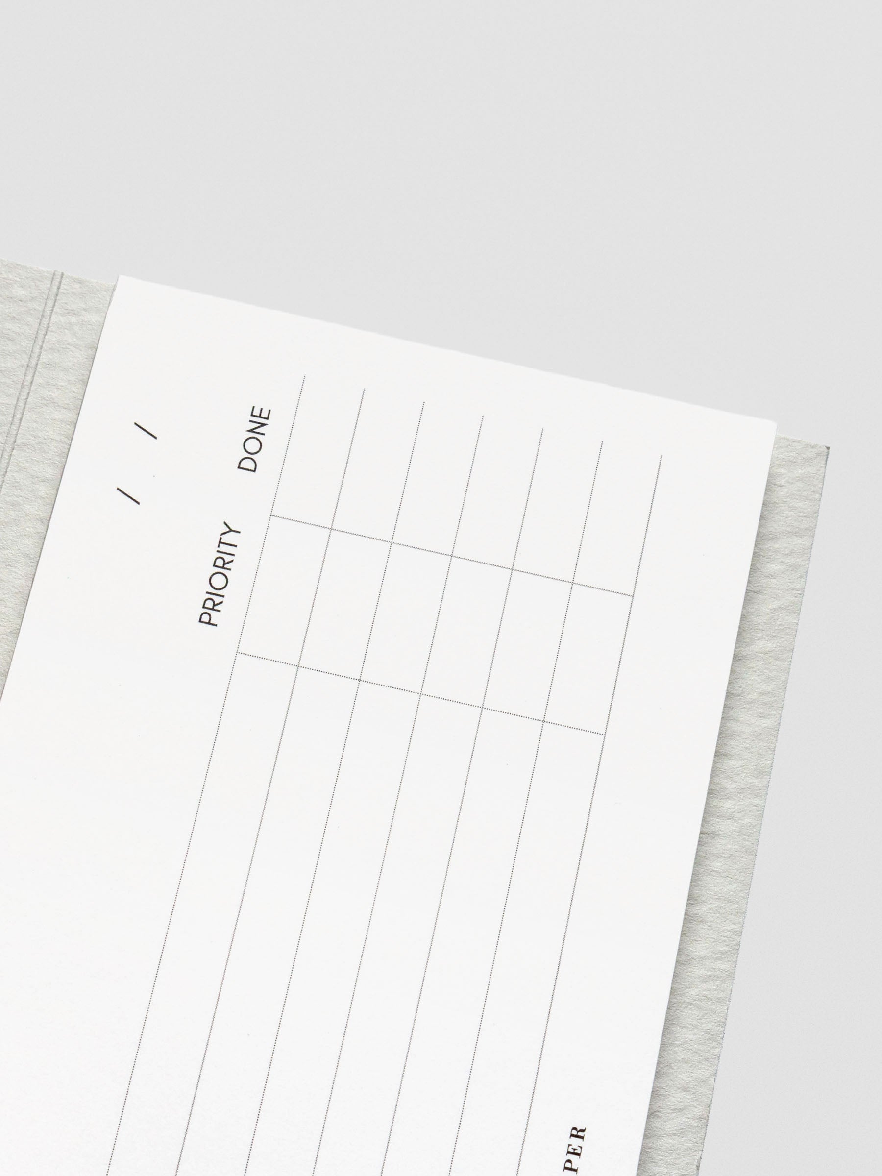 Close-up of the top portion of the notepad showing date lines and priority and done checkboxes printed in fine black ink on white paper.