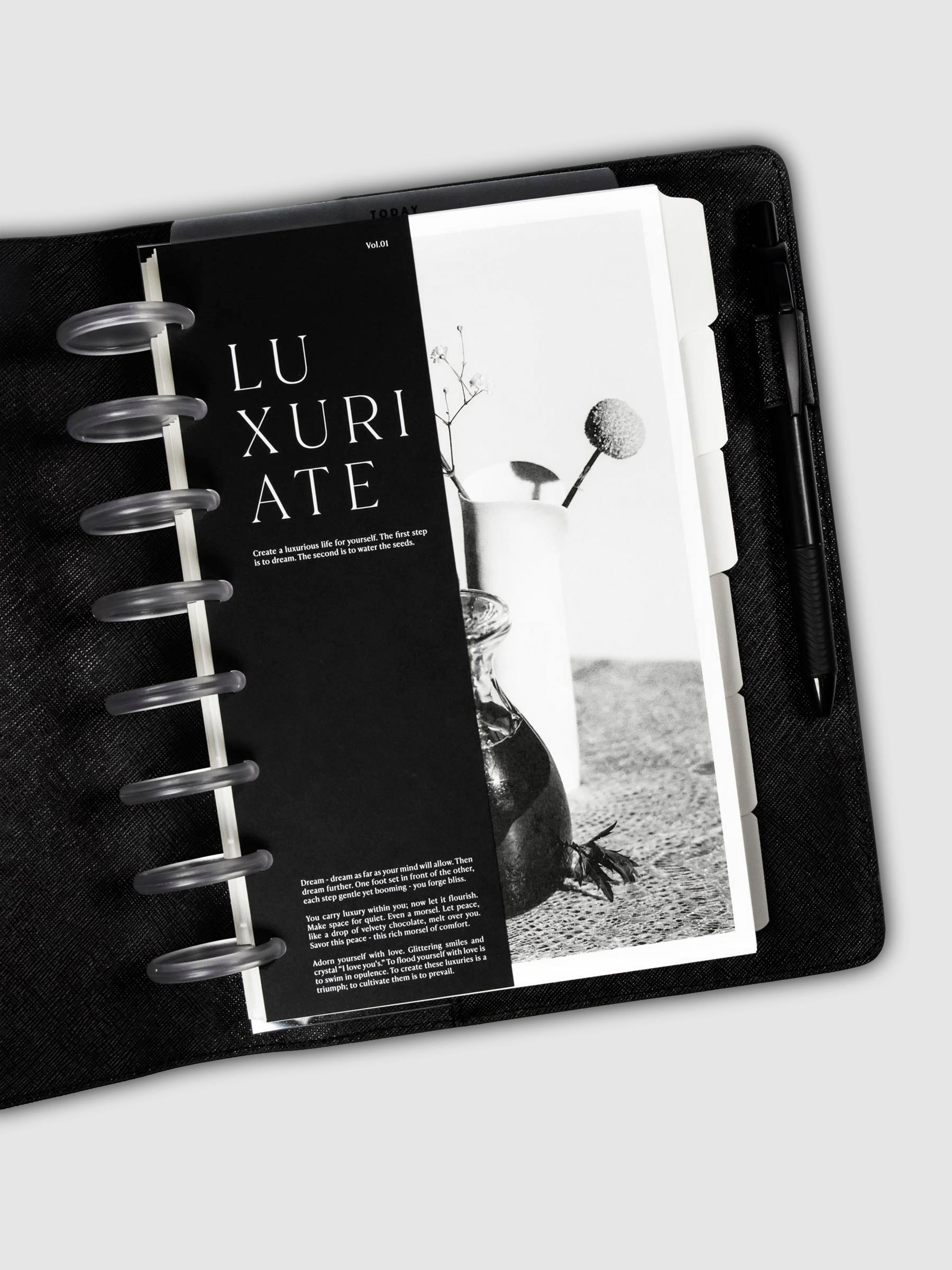 Luxuriate Planner Dashboard Duo styled inside a discbound planner tucked into a black leather agenda cover. There is a black pen in the cover's pen loop.