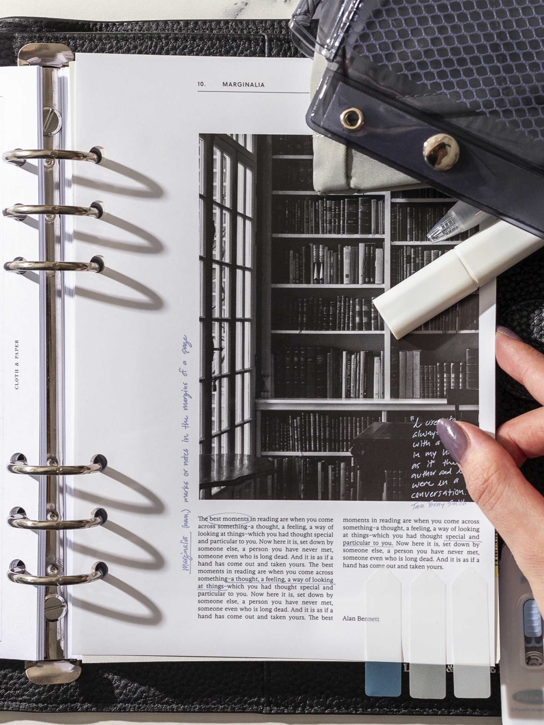 Dashboard shown in use inside a black leather planner. A hand is shown grasping the dashboard between its fingers. A pencil pouch, tape correction pen, and several page flags are also visible and frame around the dashboard.