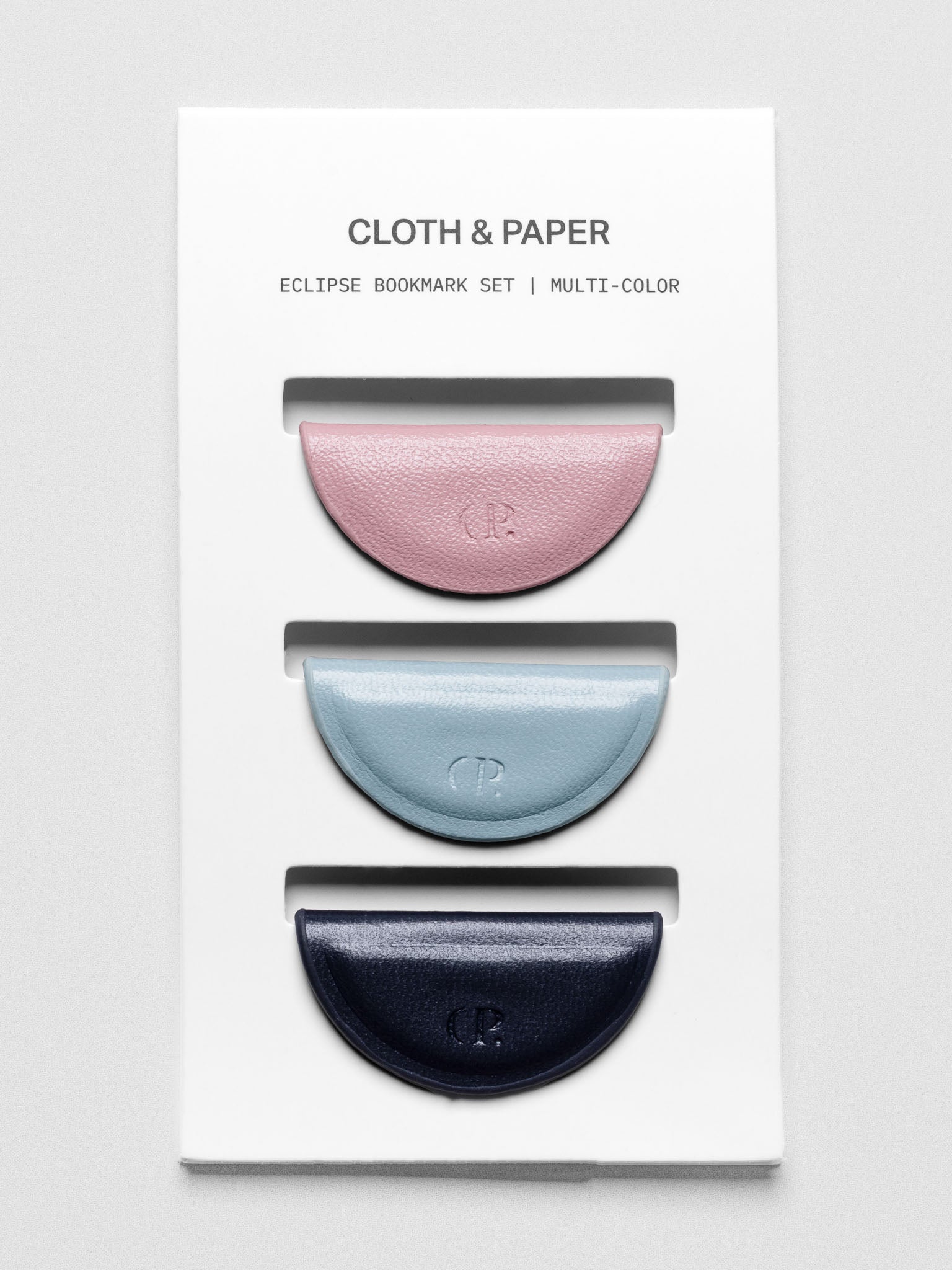 Set of three mini magnetic bookmarks in light pink, light blue, and navy blue folded in half on a backing card.