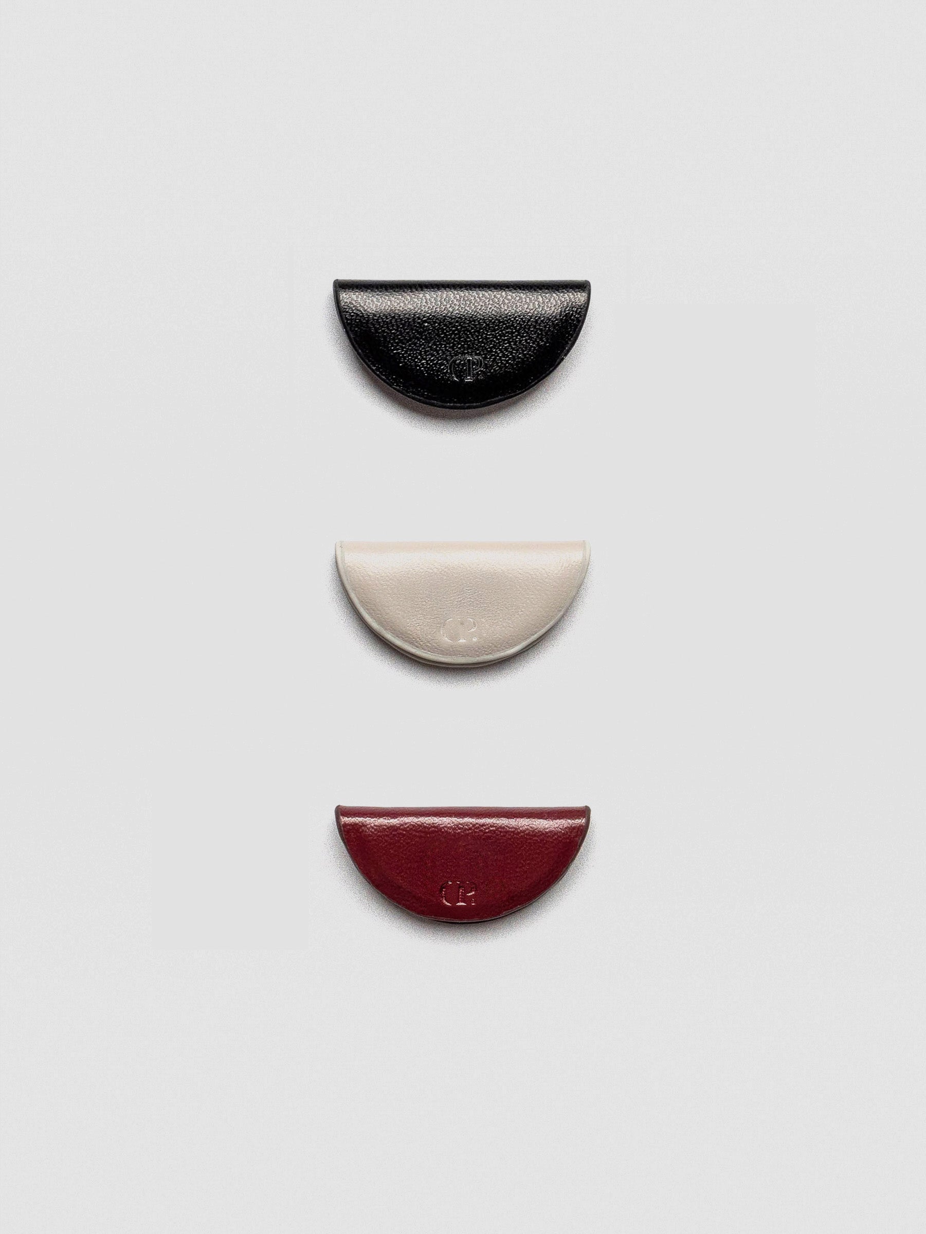 A set of three semi-circle leather magnetic bookmarks in black, cream, and burgundy colors