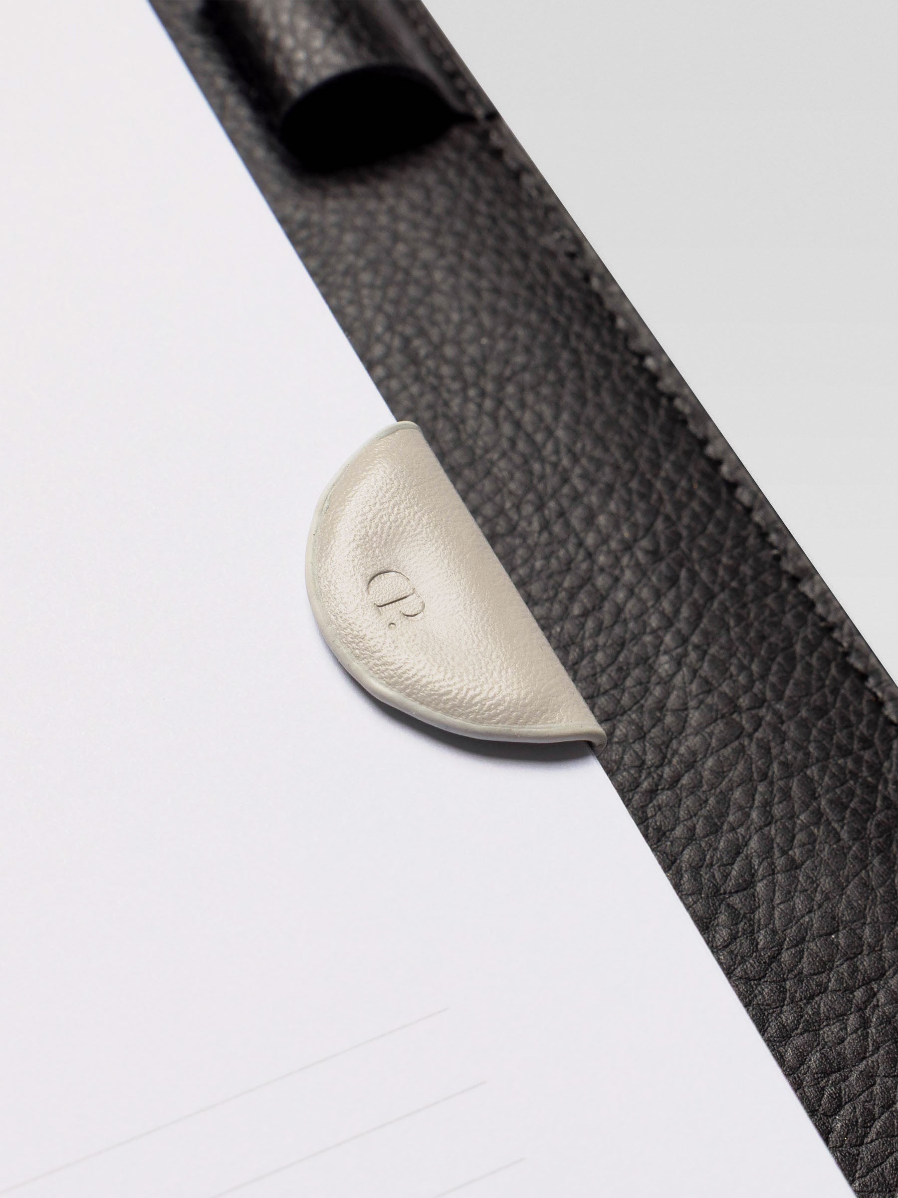 Close-up of the cream leather magnetic bookmark clipped onto a planner page with a black leather cover.