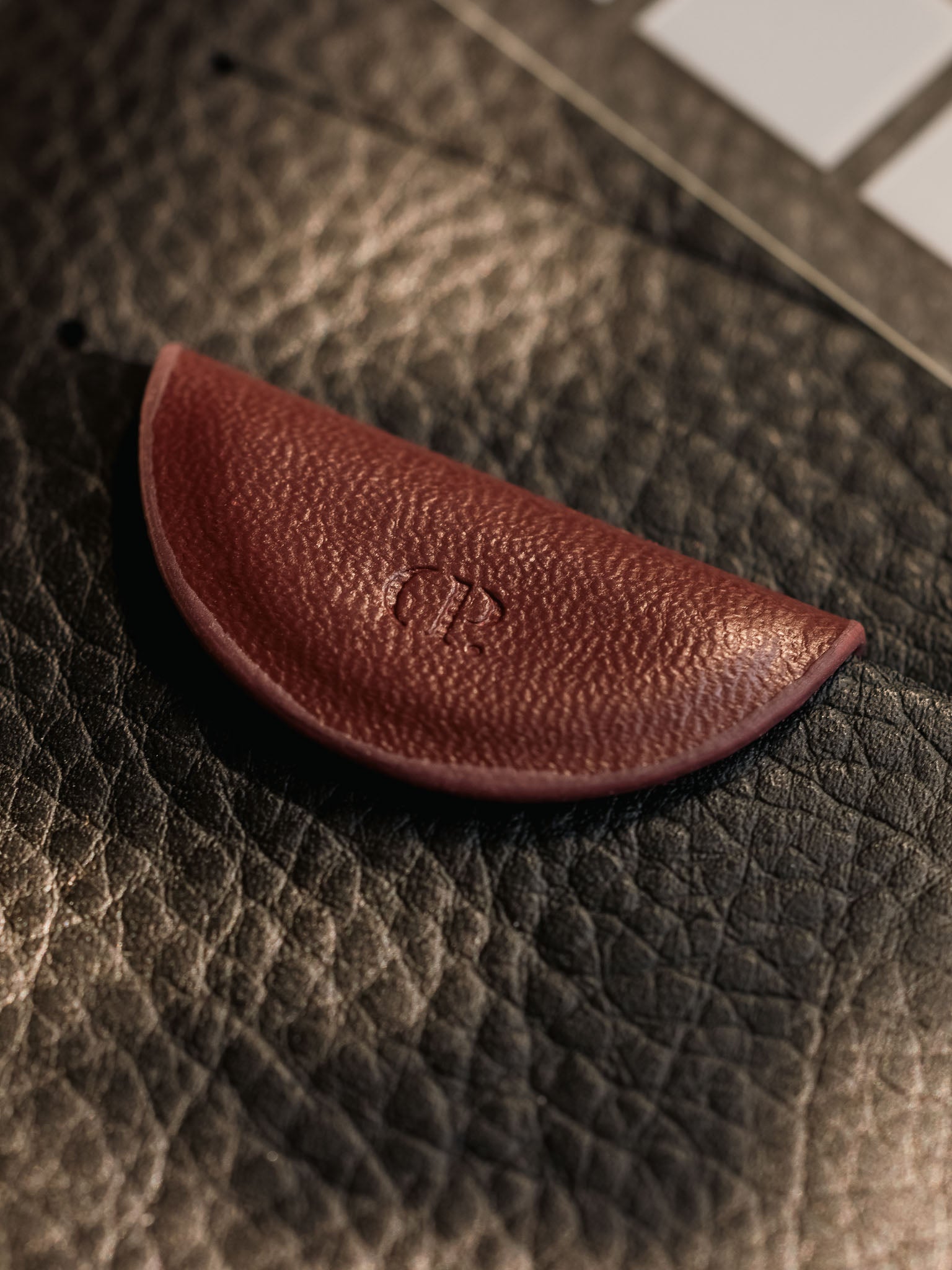 Close-up of the Bordeaux Mini eCLIPse bookmark clip resting on a textured black leather surface, showcasing the debossed CP logo.