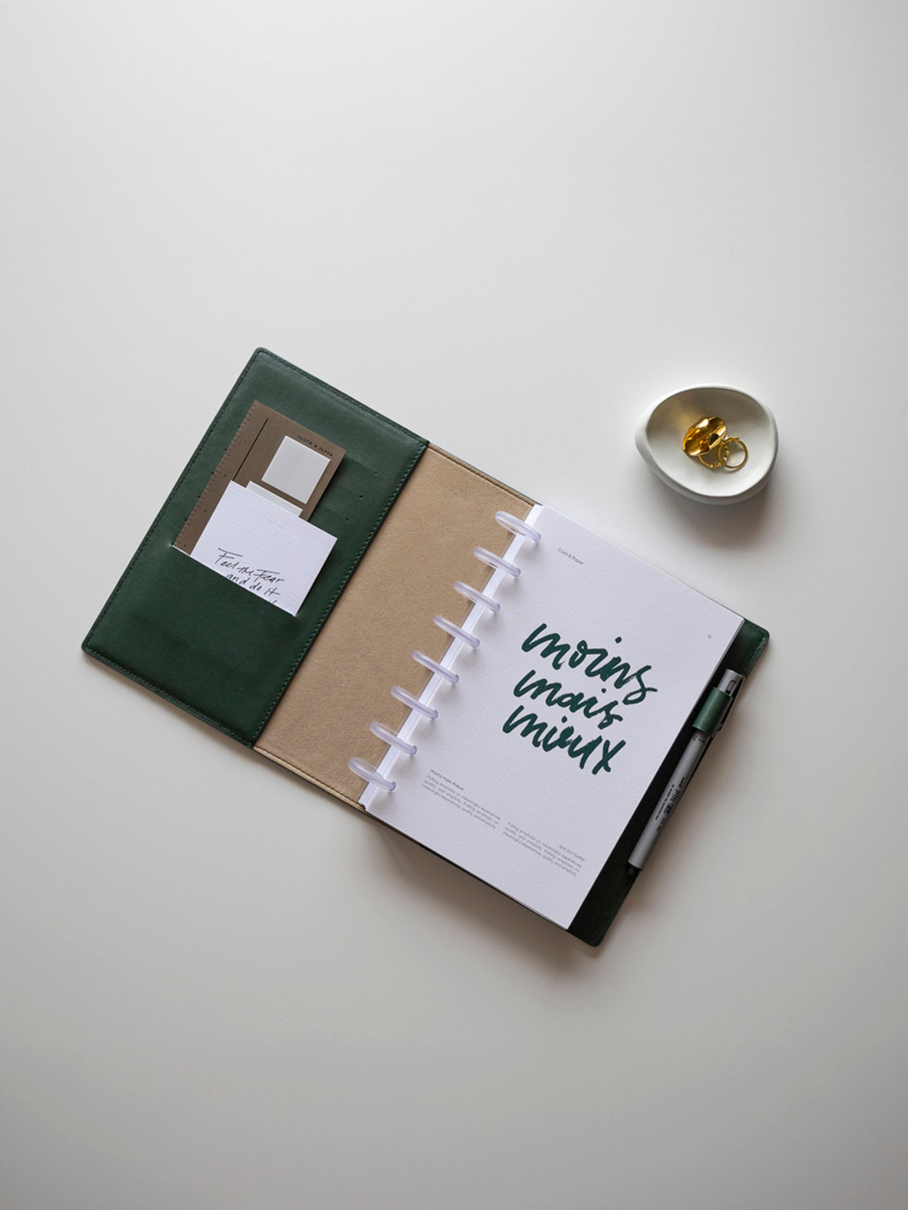 Flat lay of the stylish leather-bound disc planner with French text 'moins mais mieux' on the covers, placed on a neutral background. 